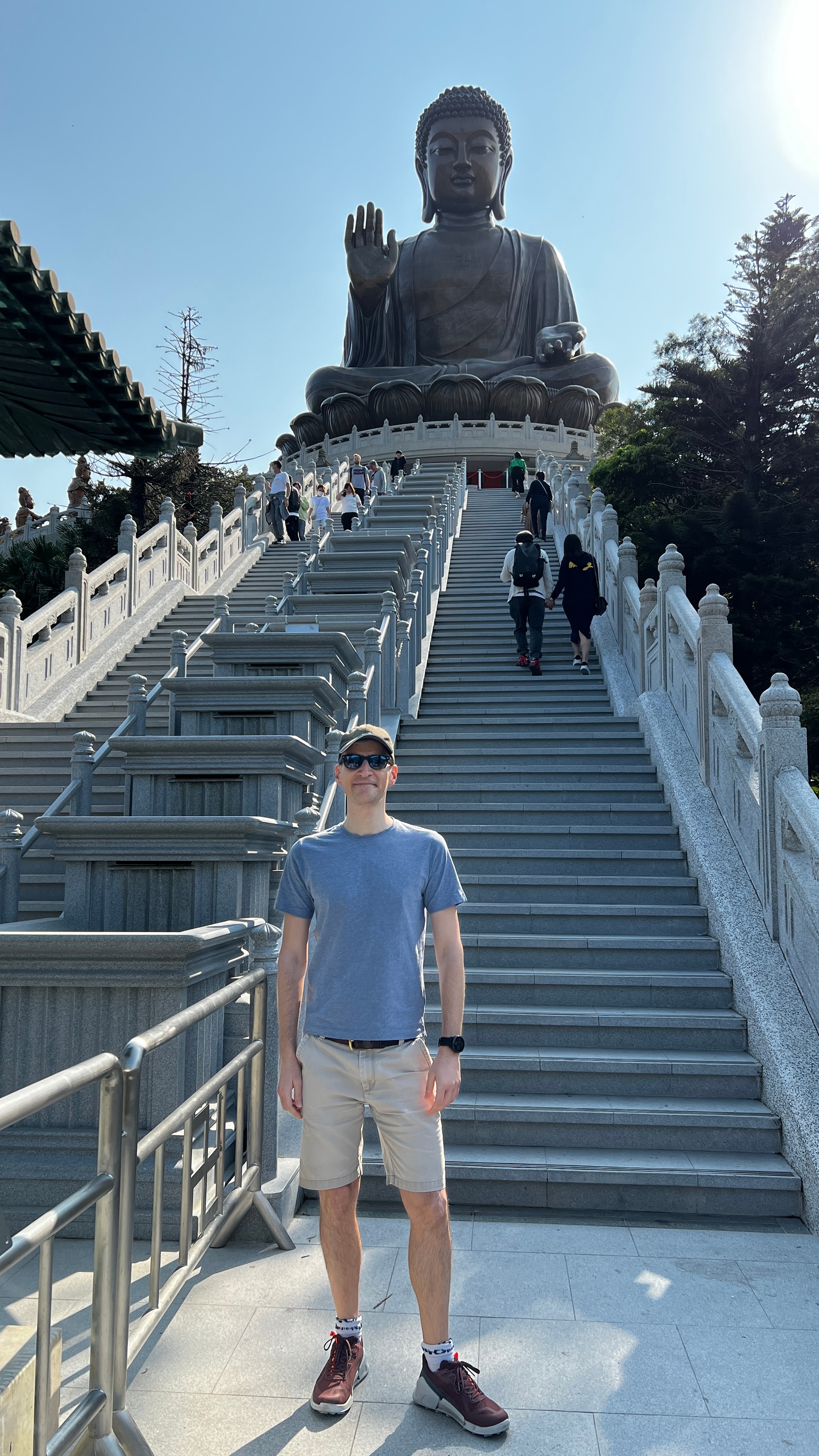 Advisor posing for an image at the bottom of a staircase with a large Buddha statue at the top