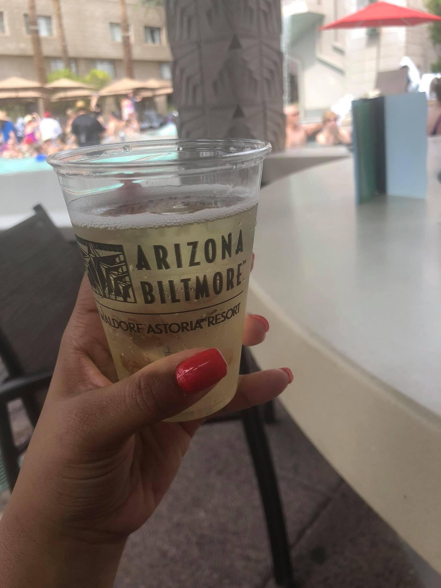 View of a hand holding a cup reading “Arizona Biltmore” with a resort pool visible in the background