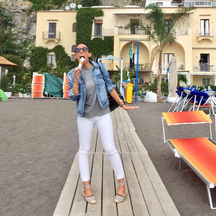 Whitney in white pants and a denim jacket eating an ice cream on the beach in Positano