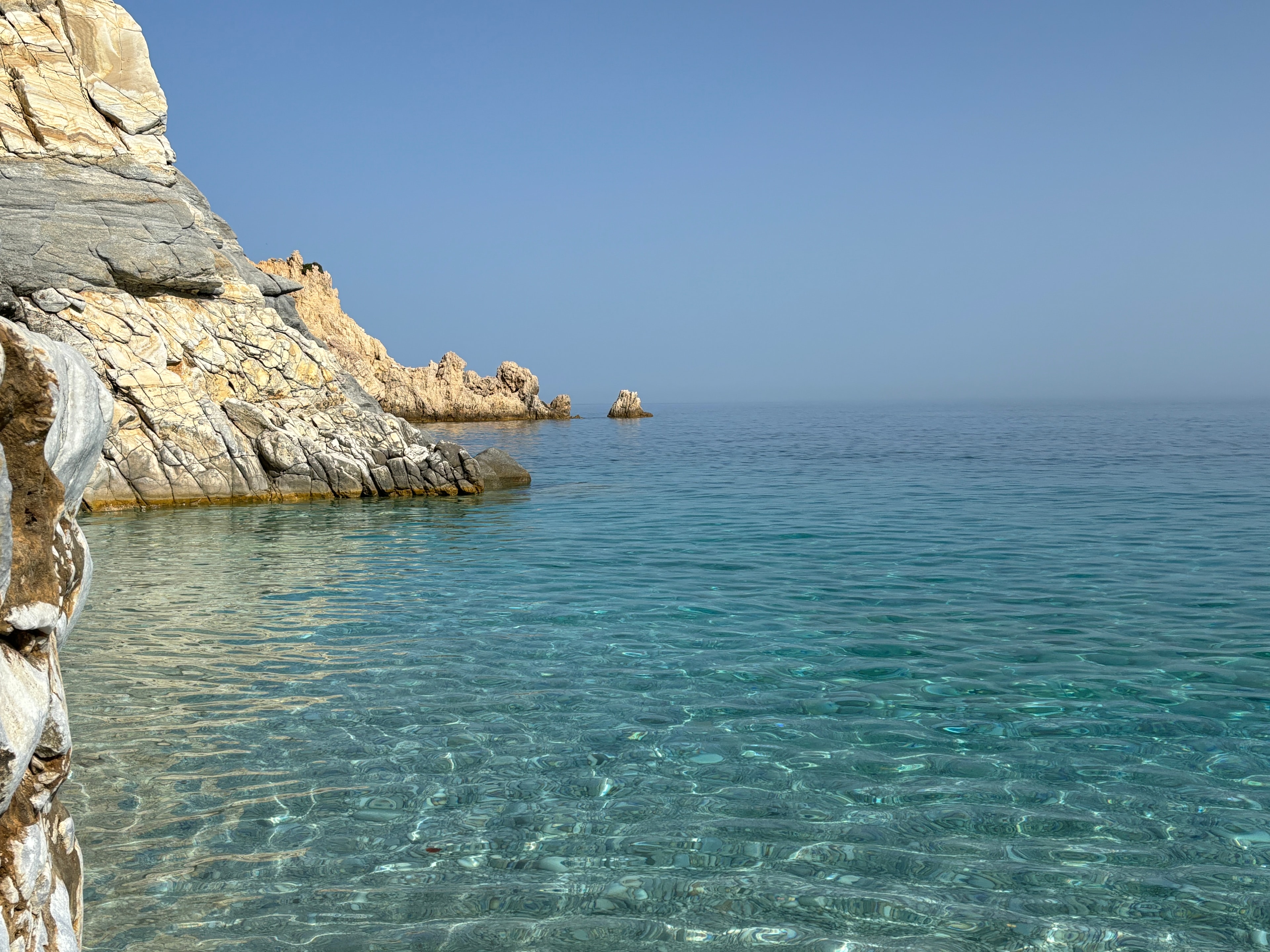 A clear blue, calm ocean side along white stone cliffs during the day.