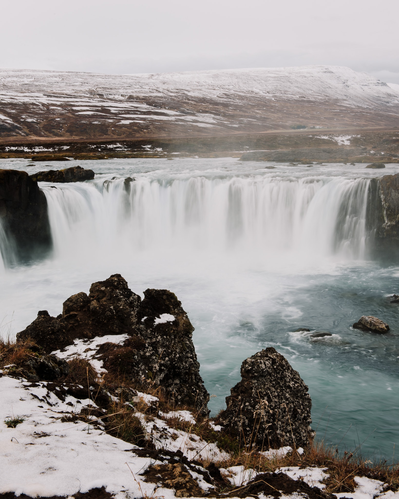 Beautiful aerial shot of a very large waterfall surrounded by an icy landscape on a cloudy day