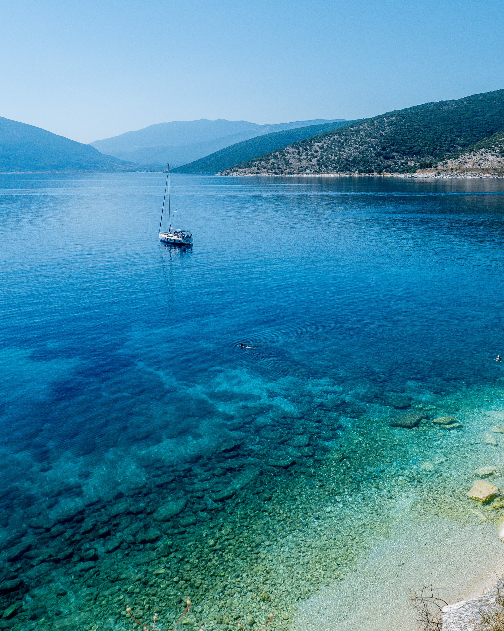 Beautiful aerial view of a calm ocean with one boat docked just offshore and mountains in the distance