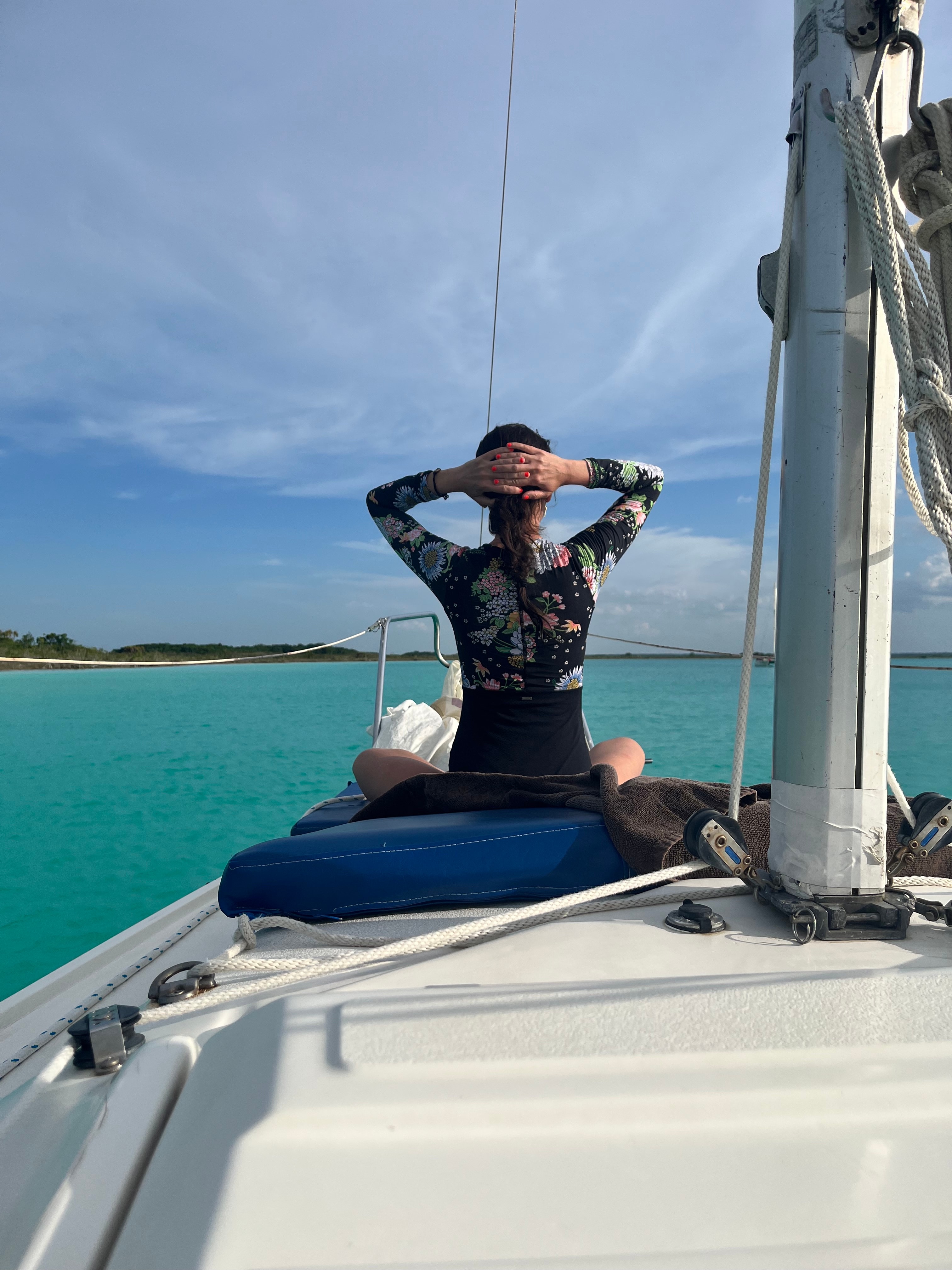 A view from behind of a woman sitting on a boat looking out at the ocean with her hands behind her head.