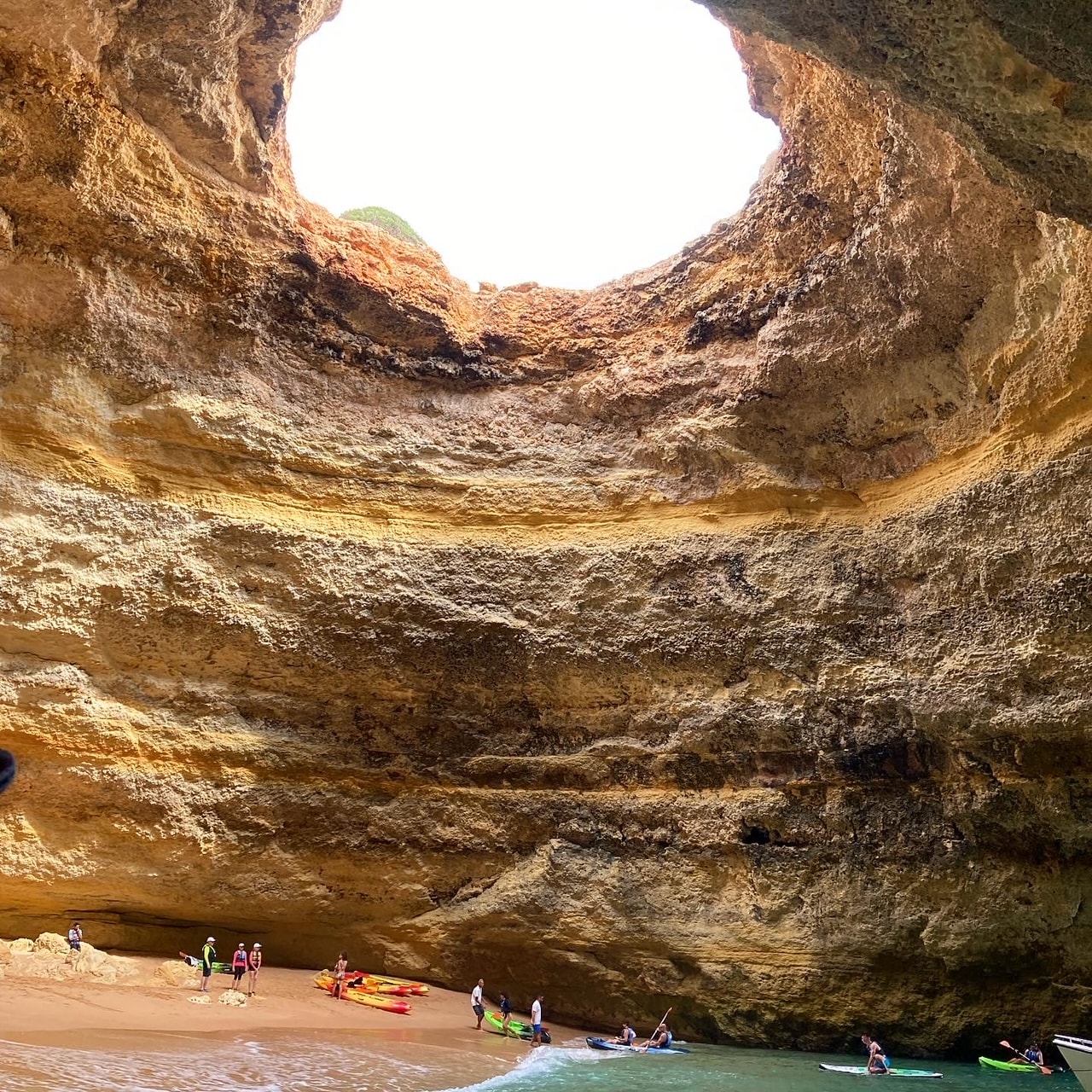 View of a small hidden beach inside a rock formation with a large hole at the top exposing the sky