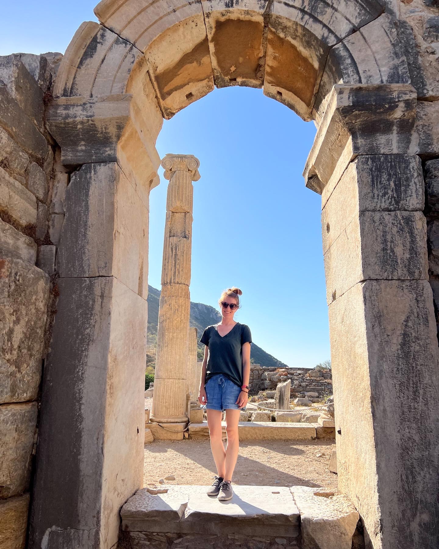 Kayla posing underneath an old stone archway near ancient ruins on a sunny day