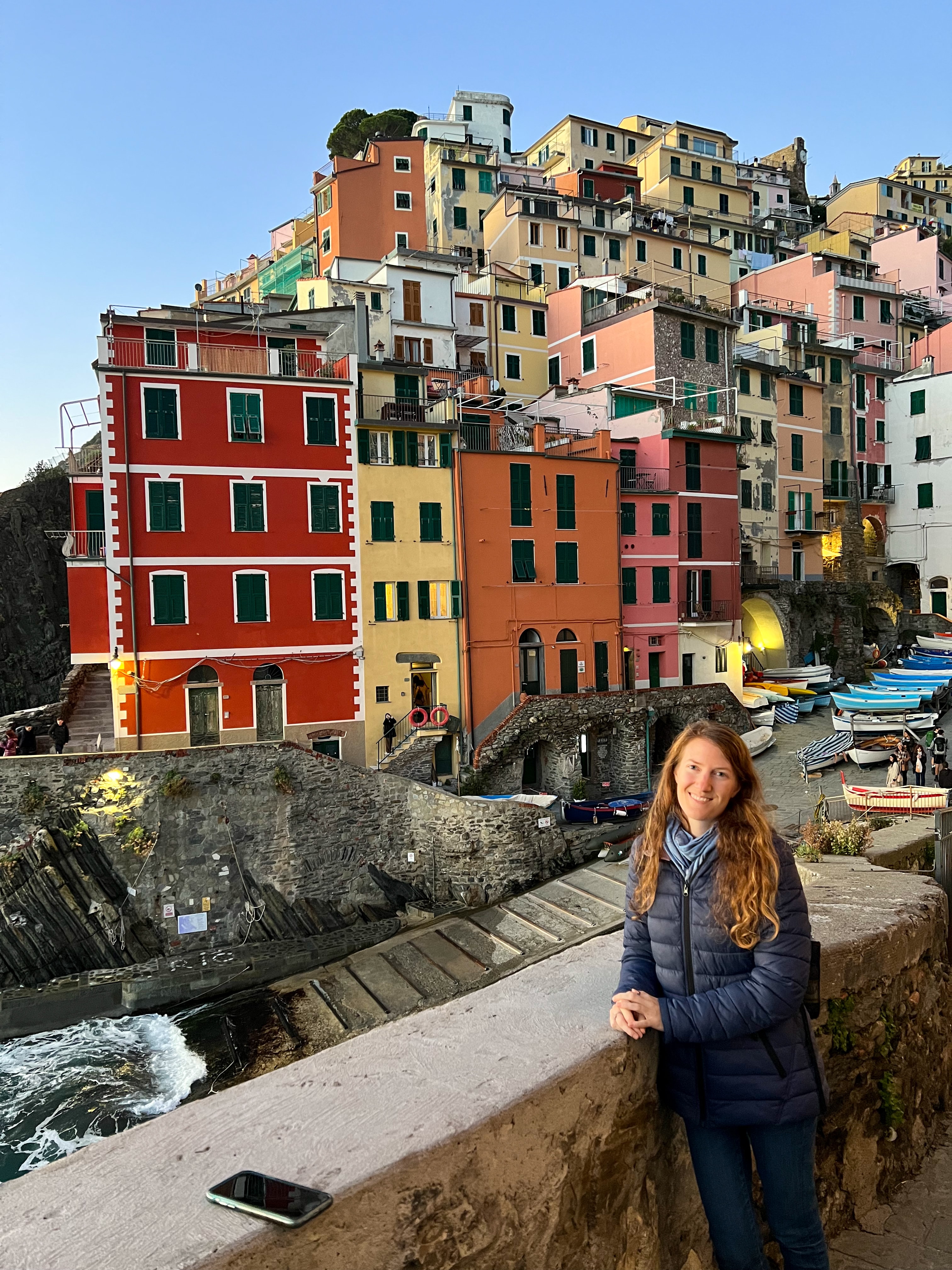 Kayla posing by a stone wall with colorful buildings visible behind her on a sunny day