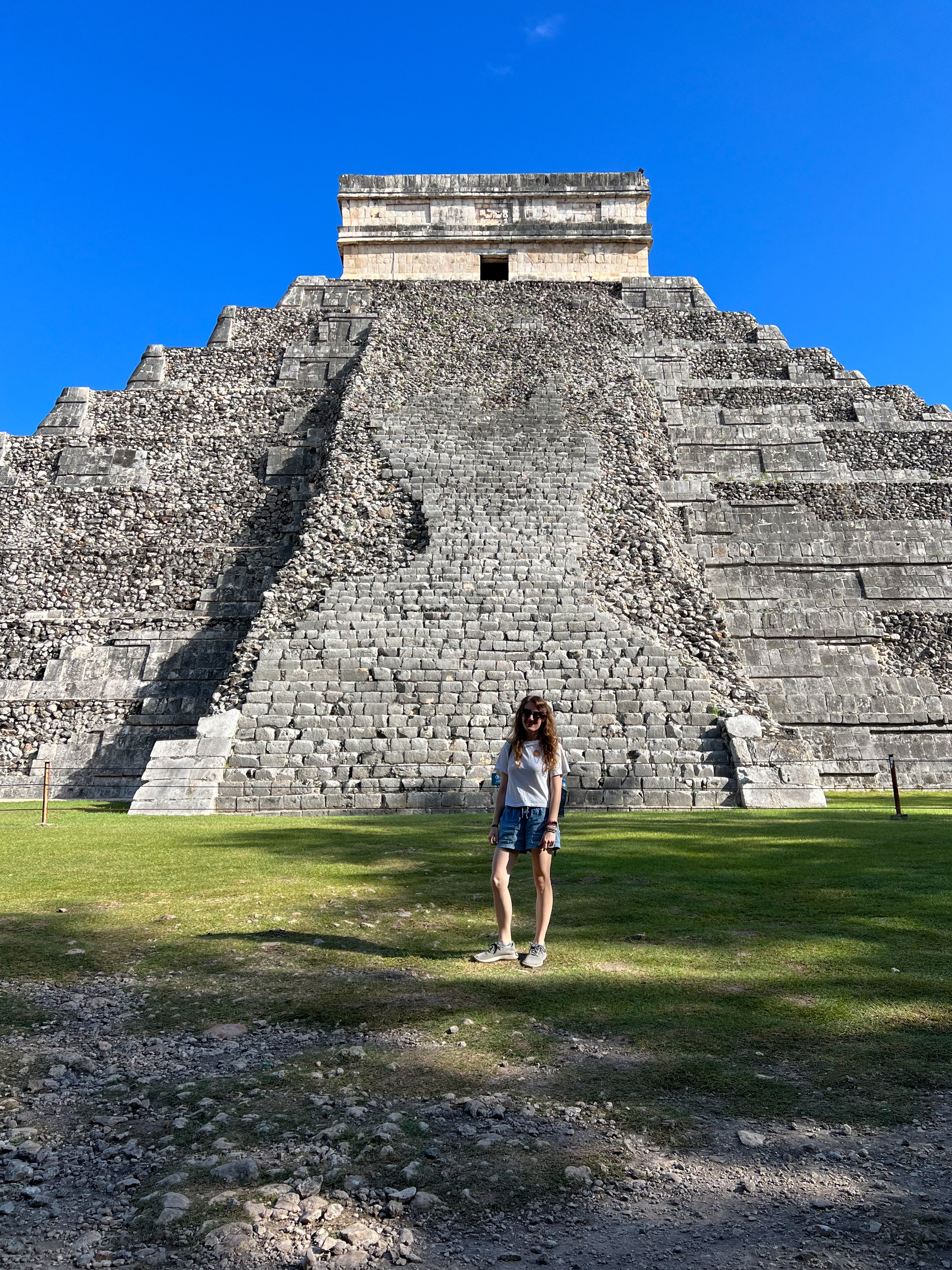 Kayla standing alone on the grass in front of an ancient pyramid under clear skies