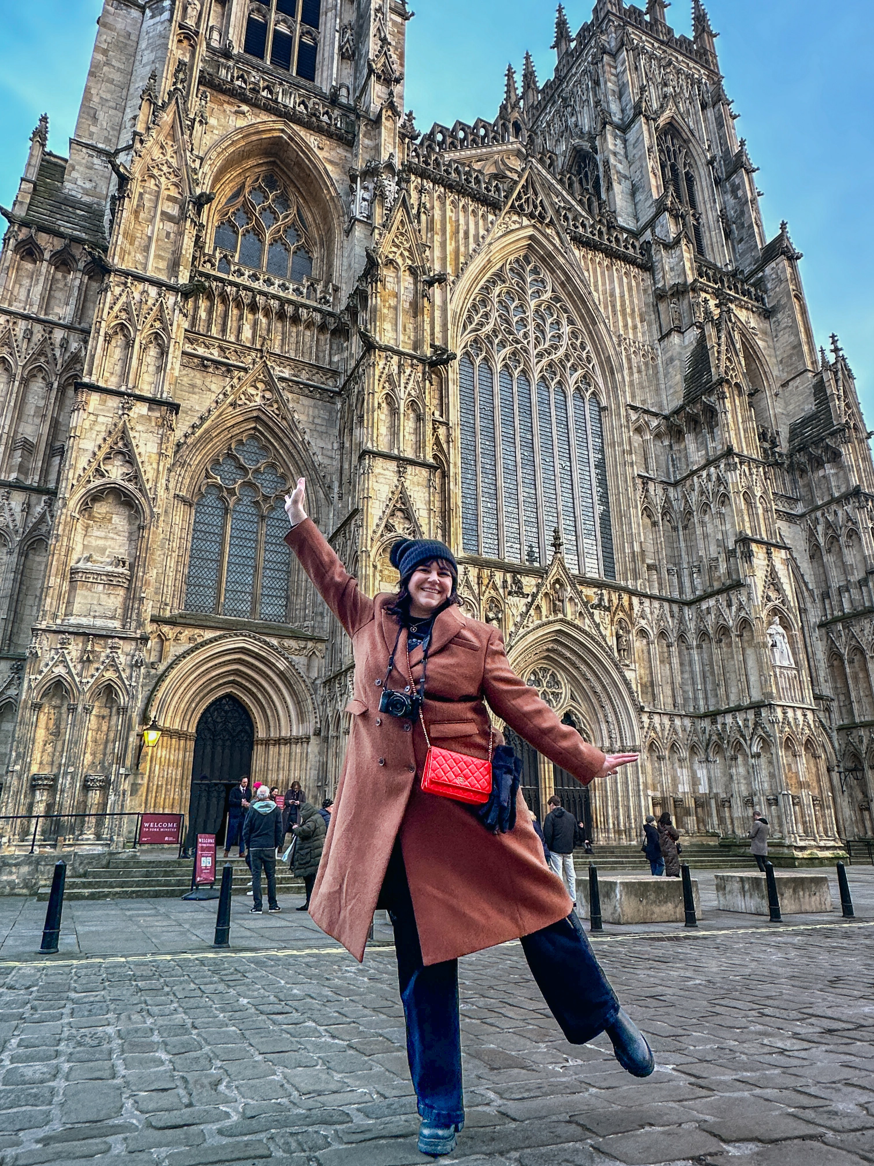 Anna in winter clothing and arm raised in front of a beautiful old cathedral on a sunny day