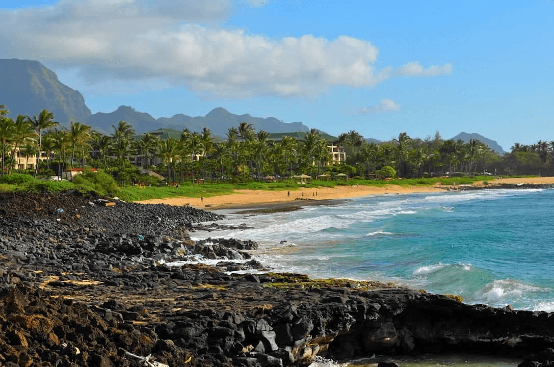 Beautiful view of a coastal area including black rocks and an empty beach with mountains visible in the distance