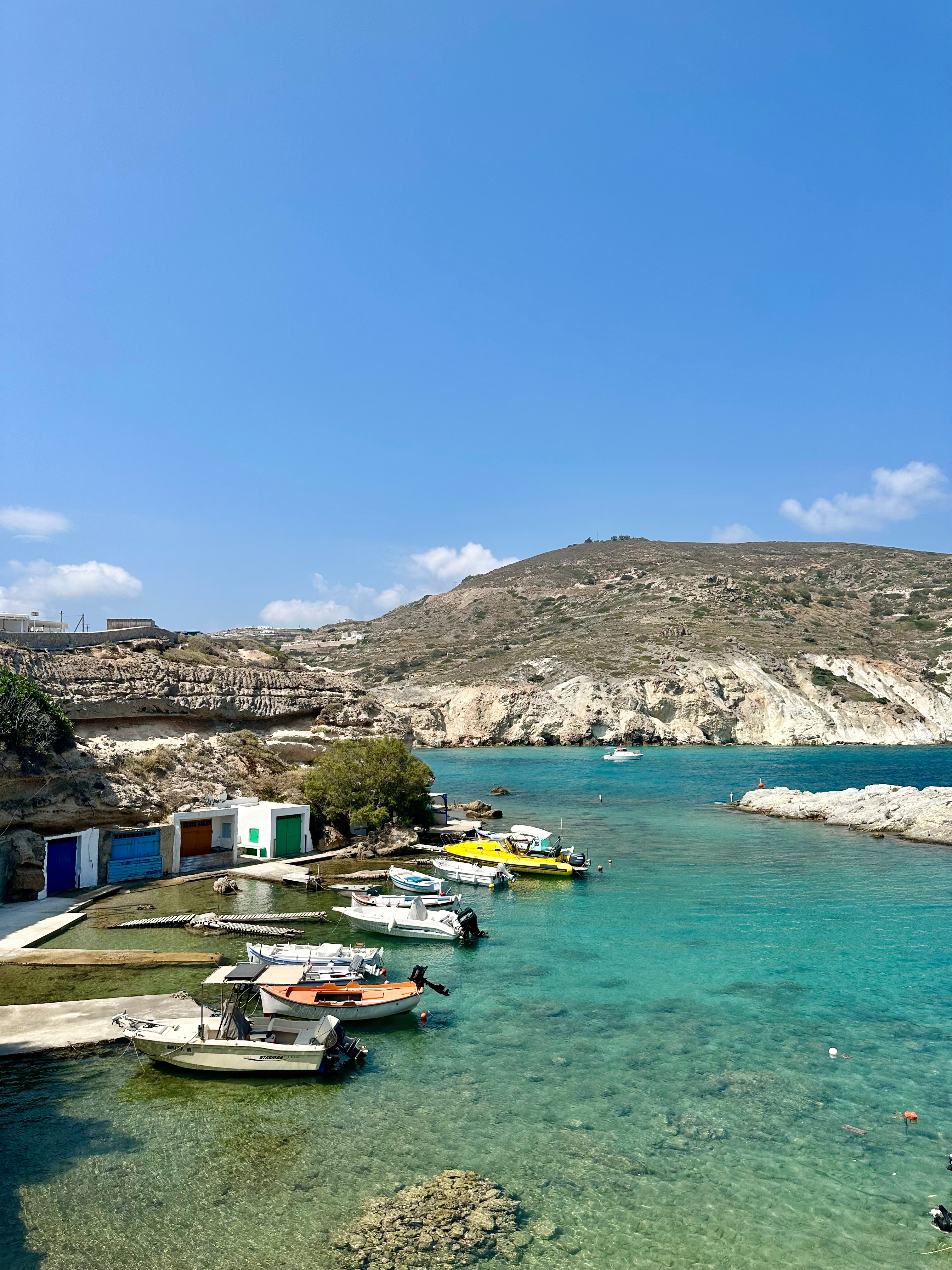 View of clear ocean water near a rocky coastline and several small boats under clear skies