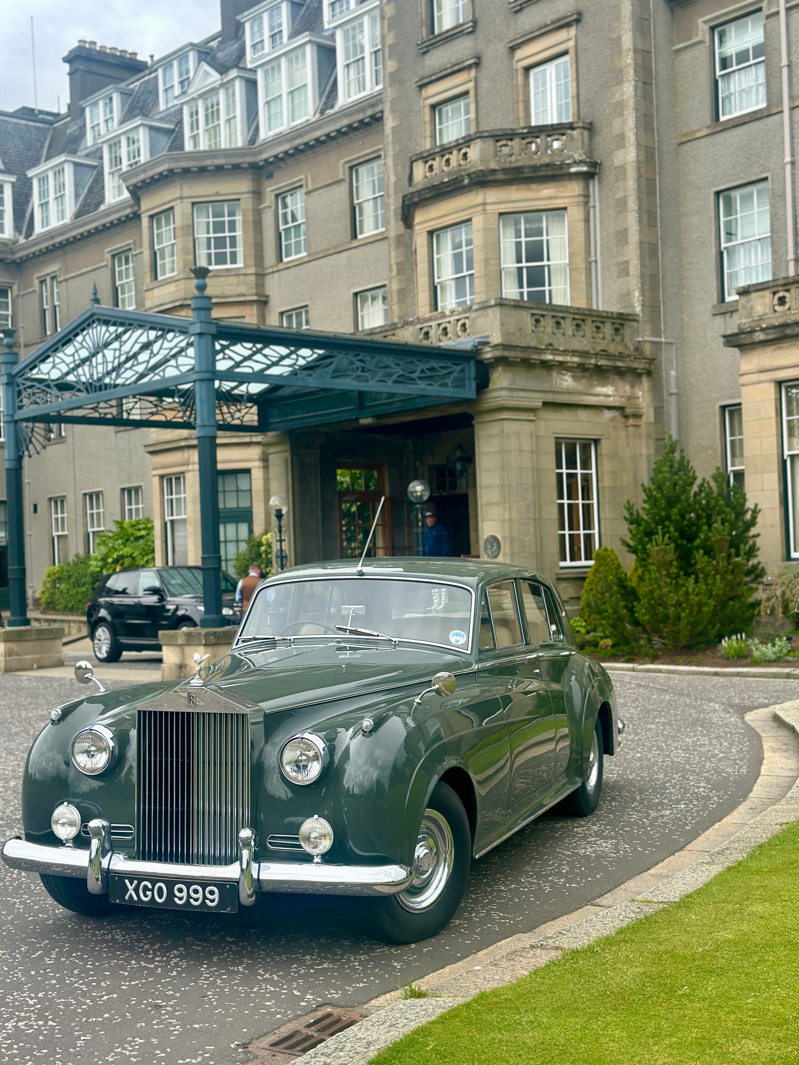 View of an old-fashioned green car parked in front of the entrance to a grand hotel