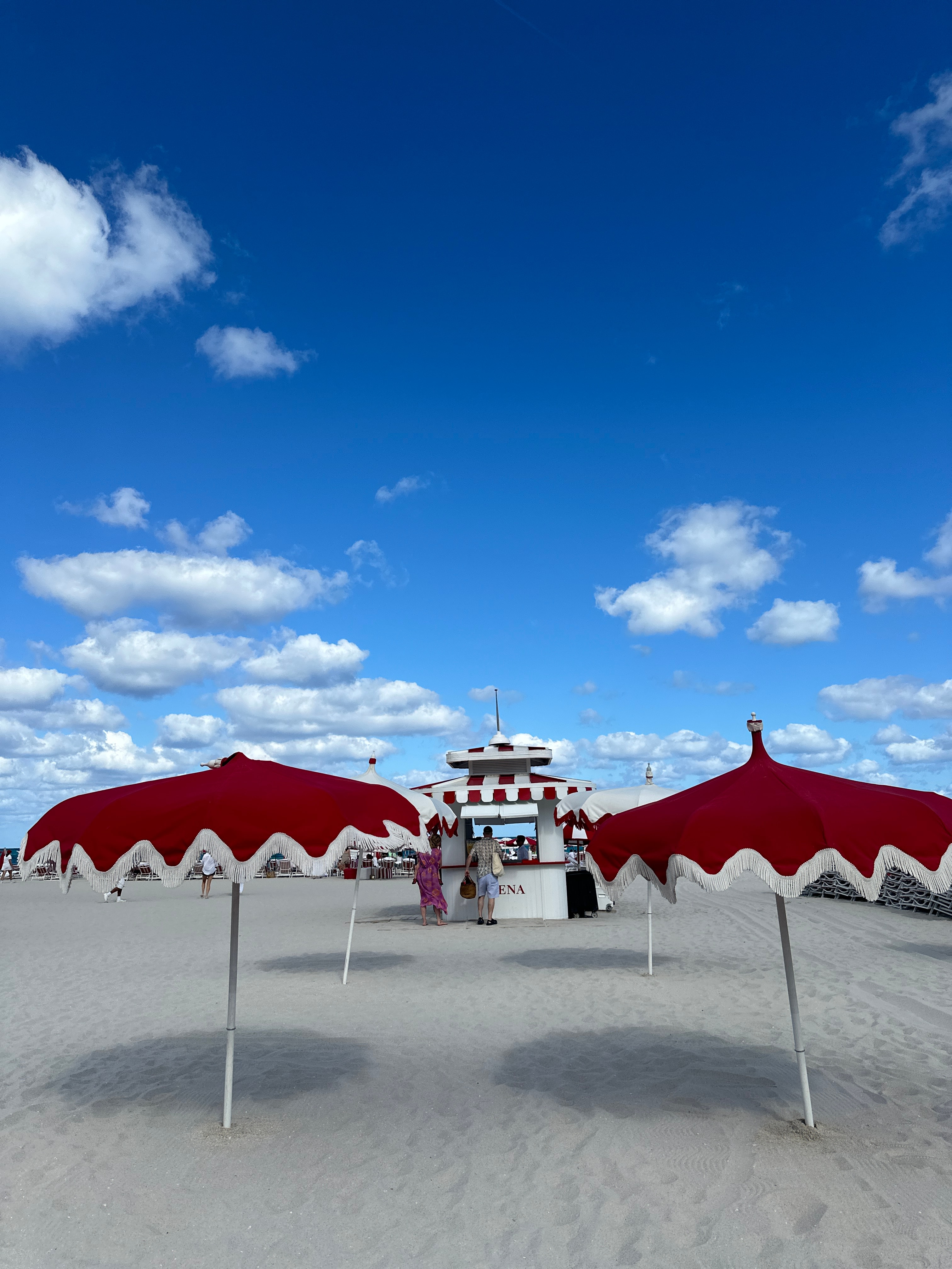 Two red and white umbrellas in the sand on a clean white sand beach under sunny skies