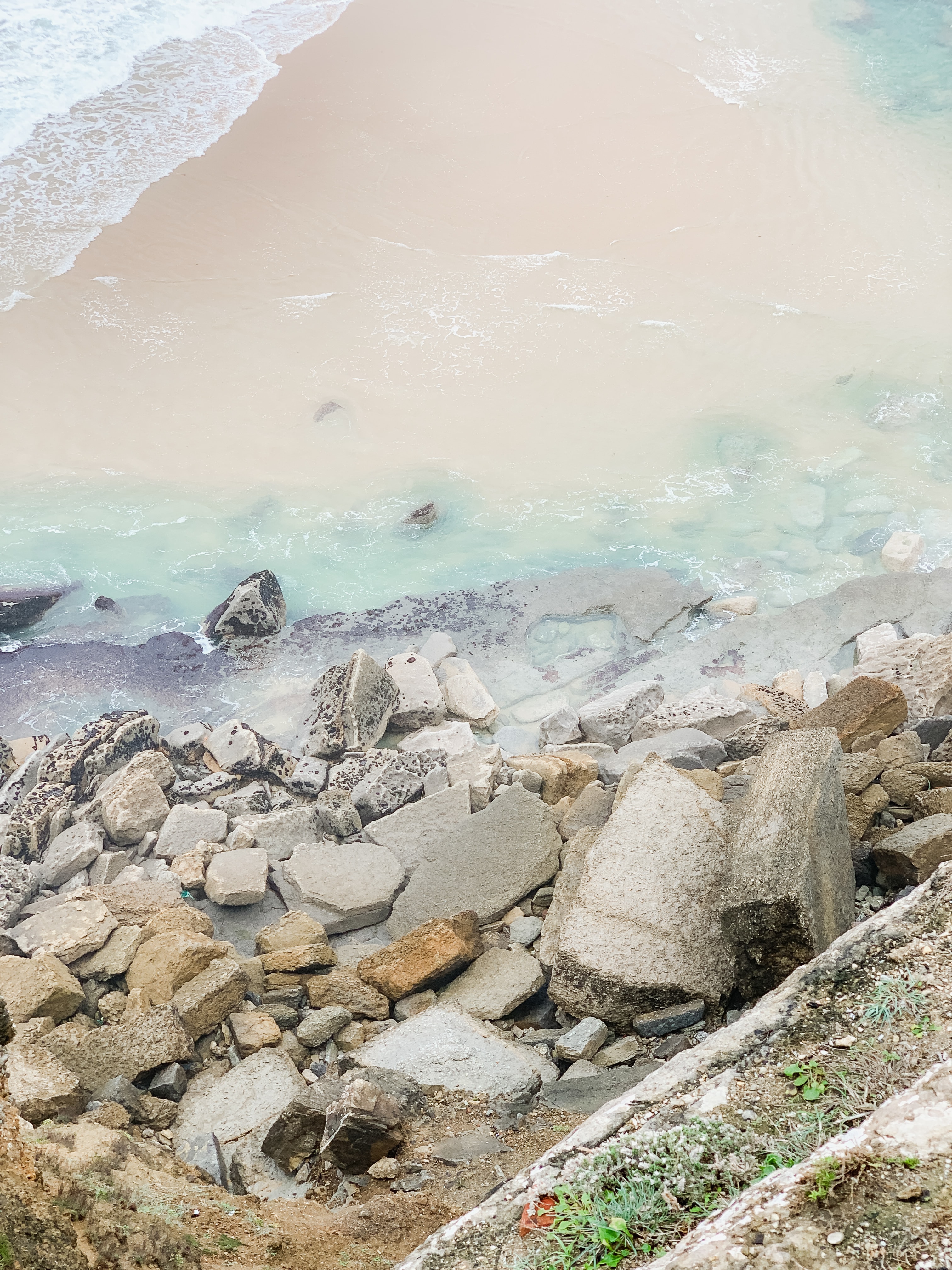 A view overlooking the beach and calm waves with cement blocks along the bluff.