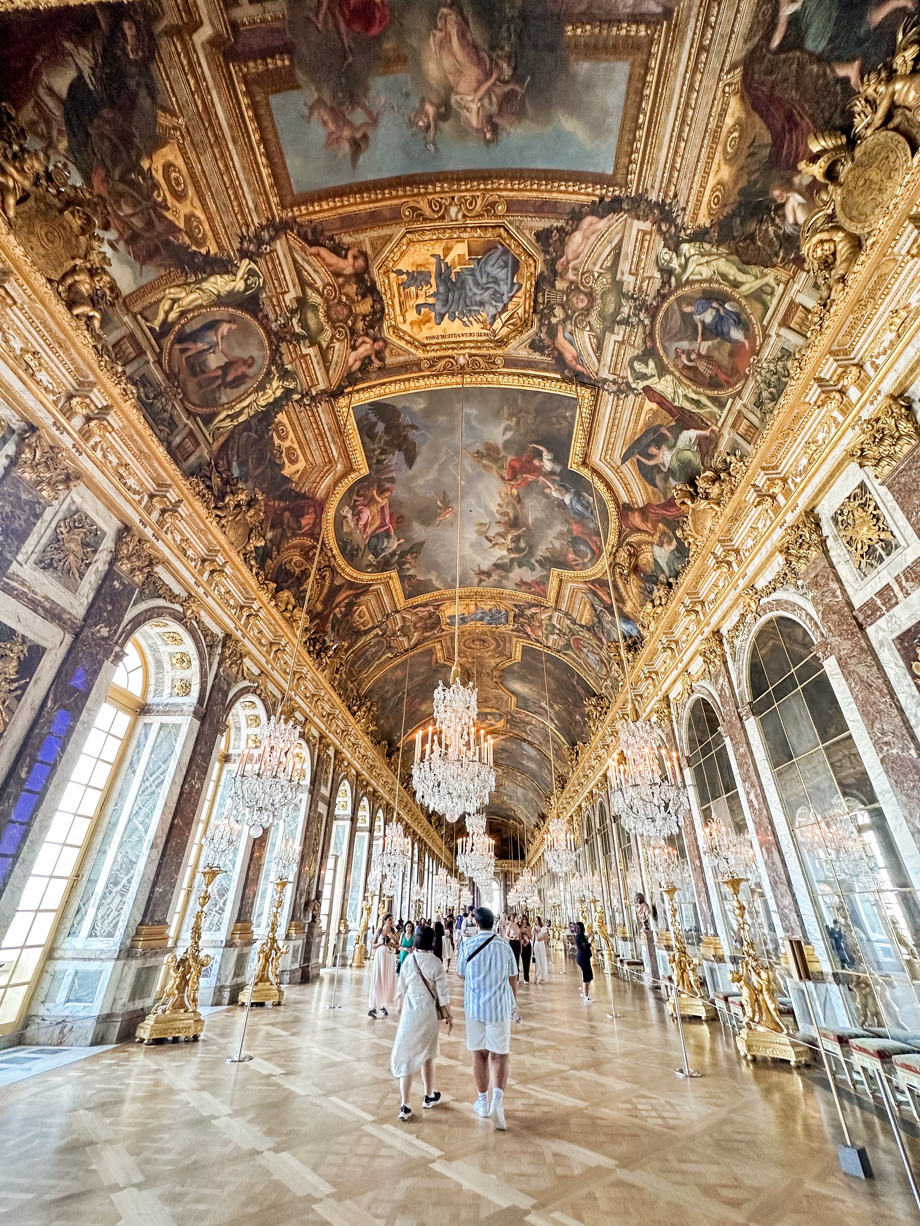 Travel advisor posing in a large hallway with arches, golden walls and ceilings covered in murals.