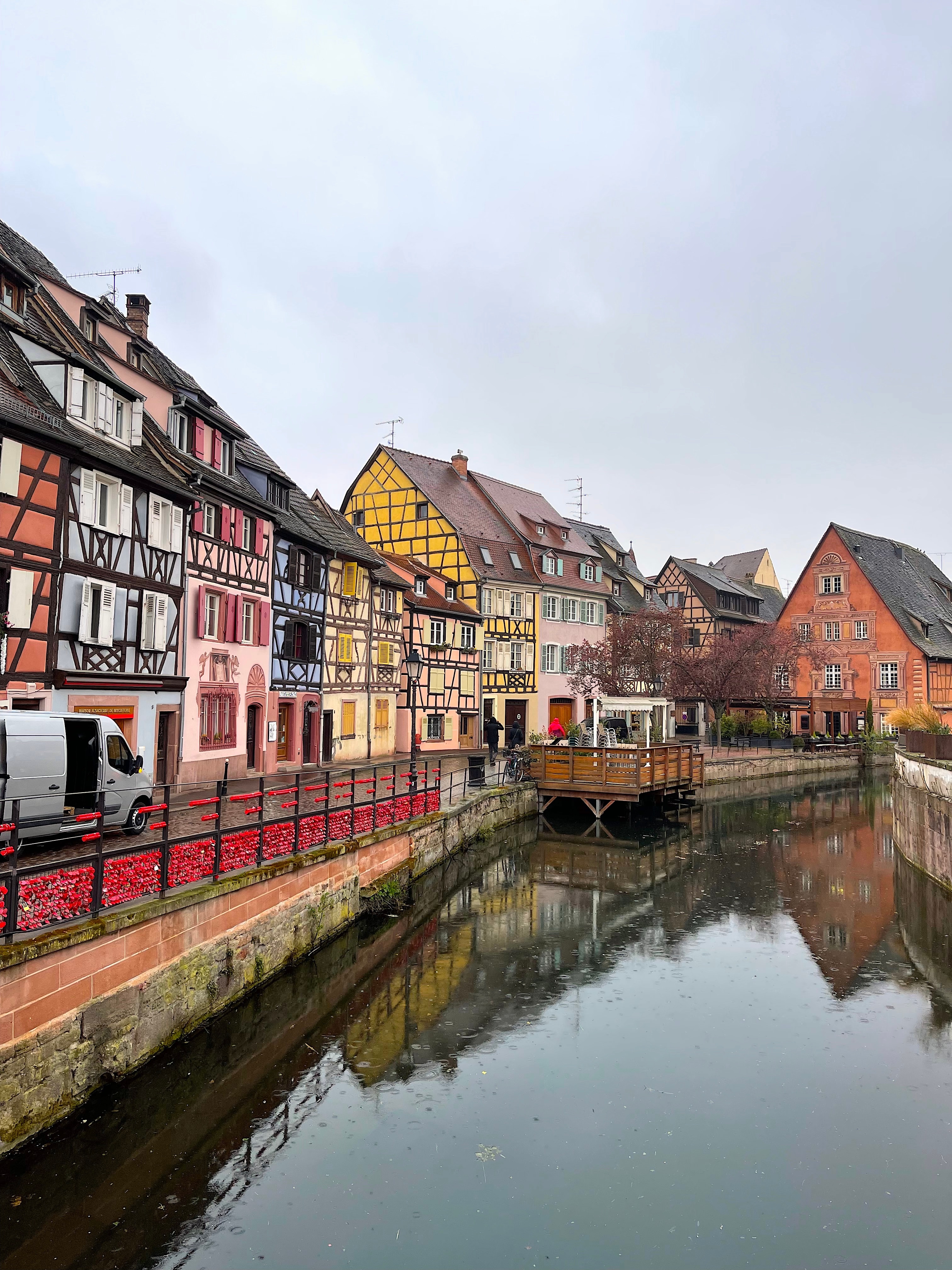 View of colorful buildings along a glassy canal under cloudy skies