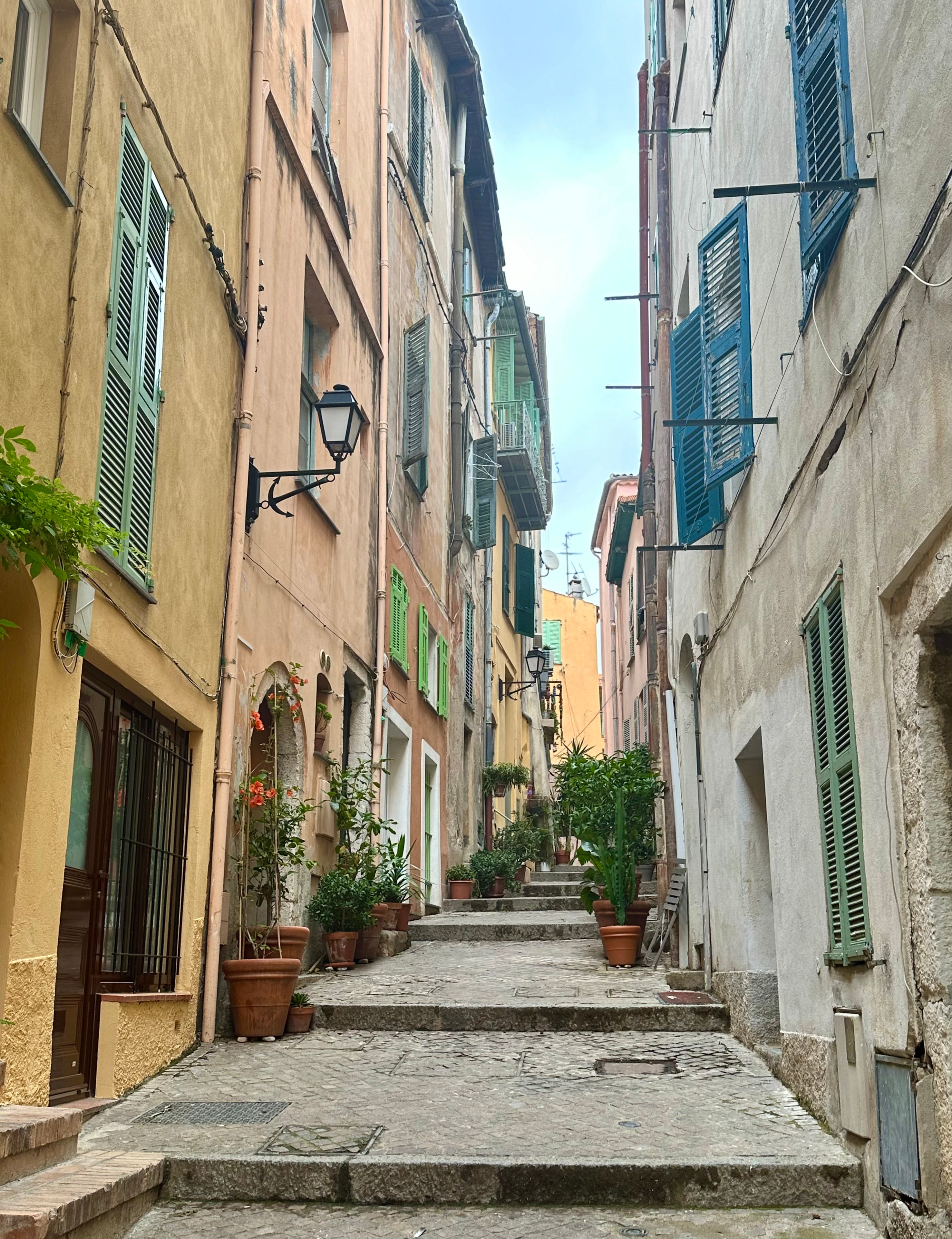 Stone path lined with blue shutters on the windows of buildings in a picturesque narrow street.