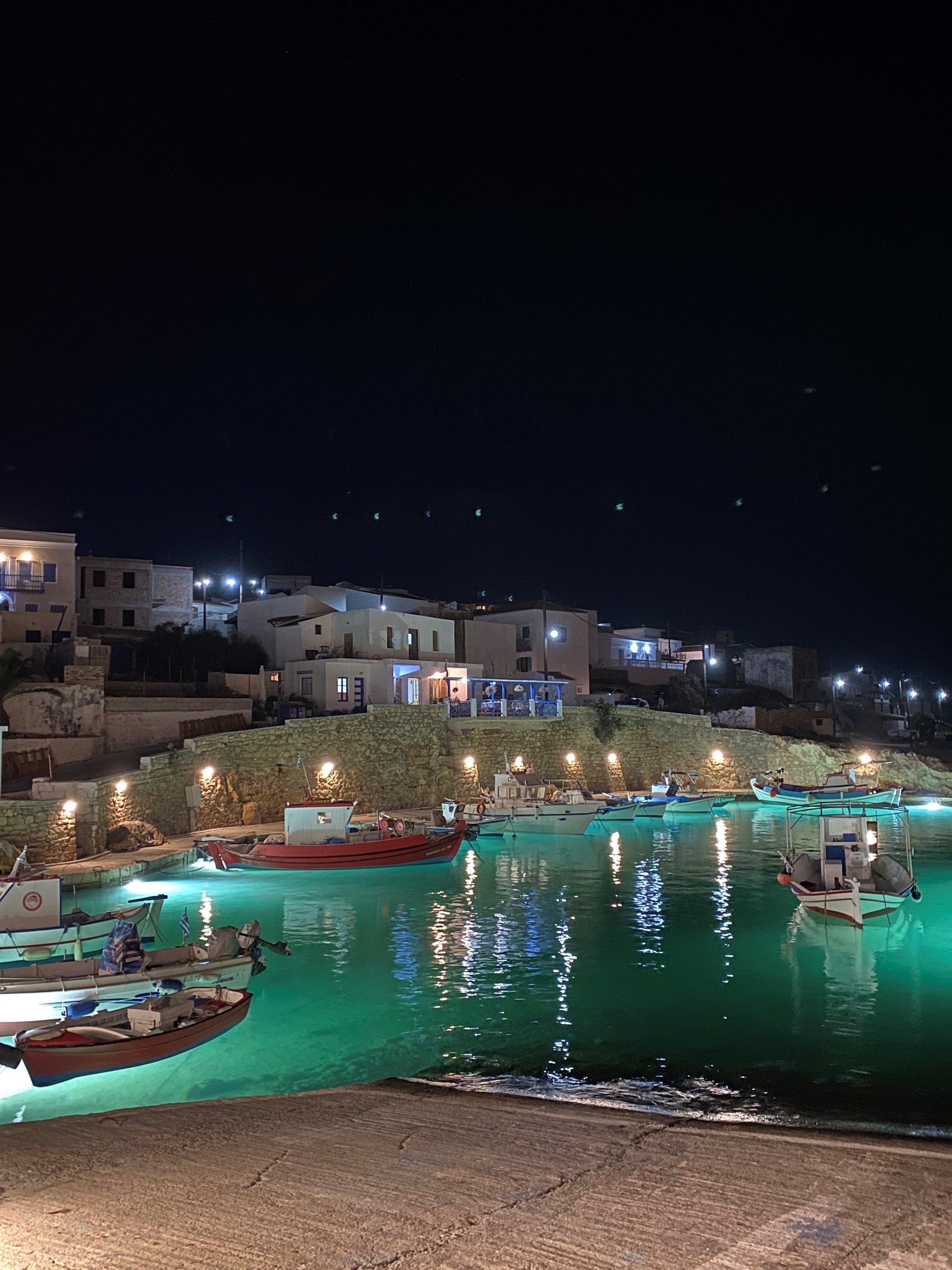 View of a marina area with small docked boats and lights underneath the water at night