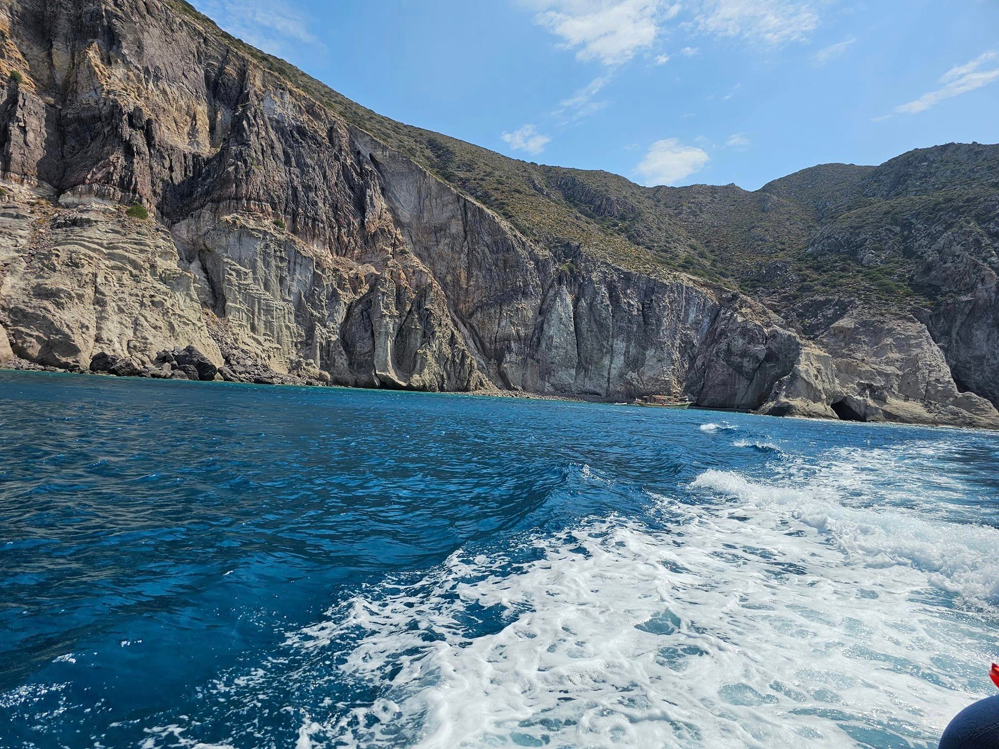 Waves lap a rocky shore on a bright day dotted with clouds. 