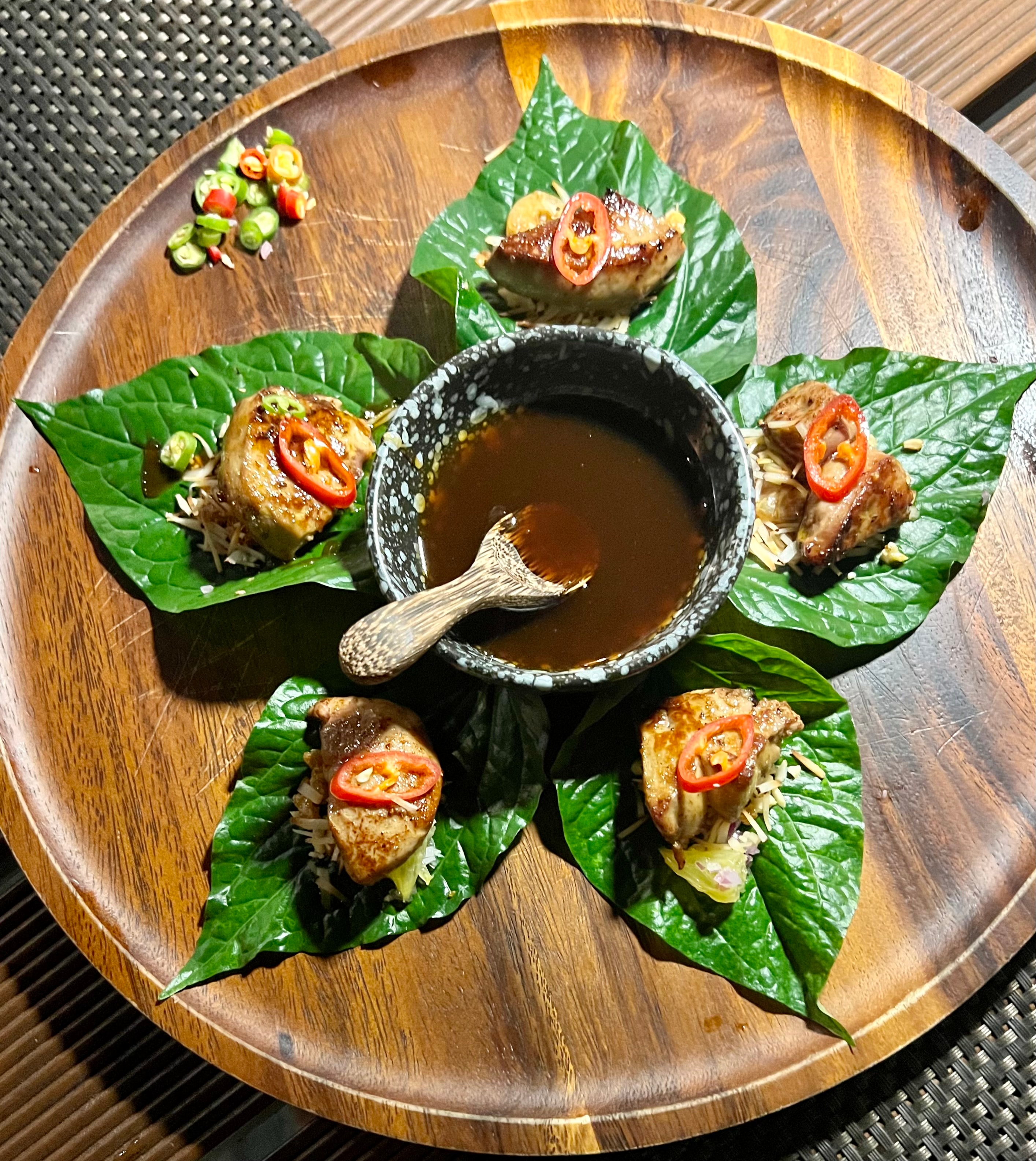 View of a wooden plate of food with a dish of sauce in the center