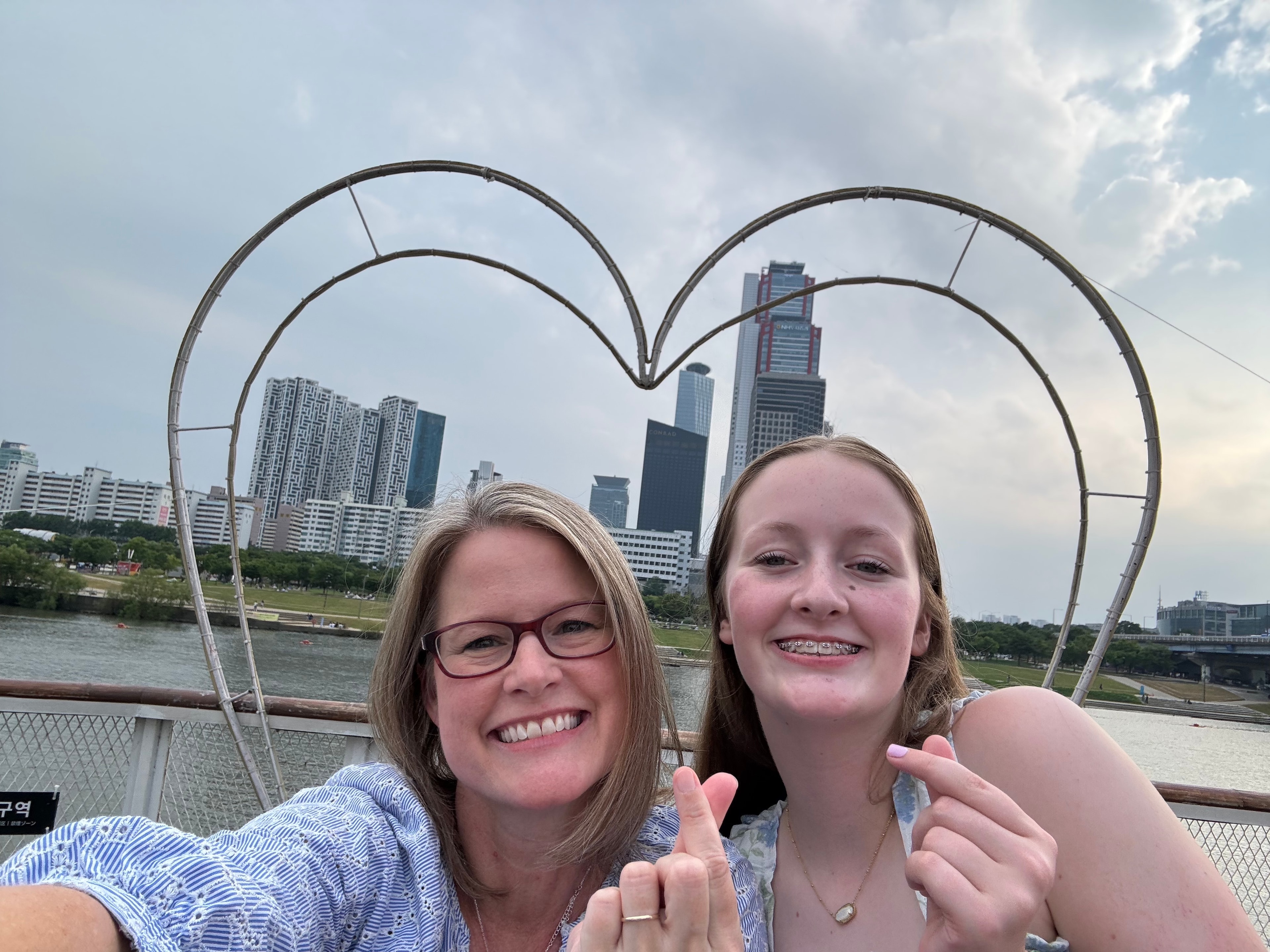 Advisor and her daughter taking a selfie in front of a heart-shaped structure with city buildings visible in the distance