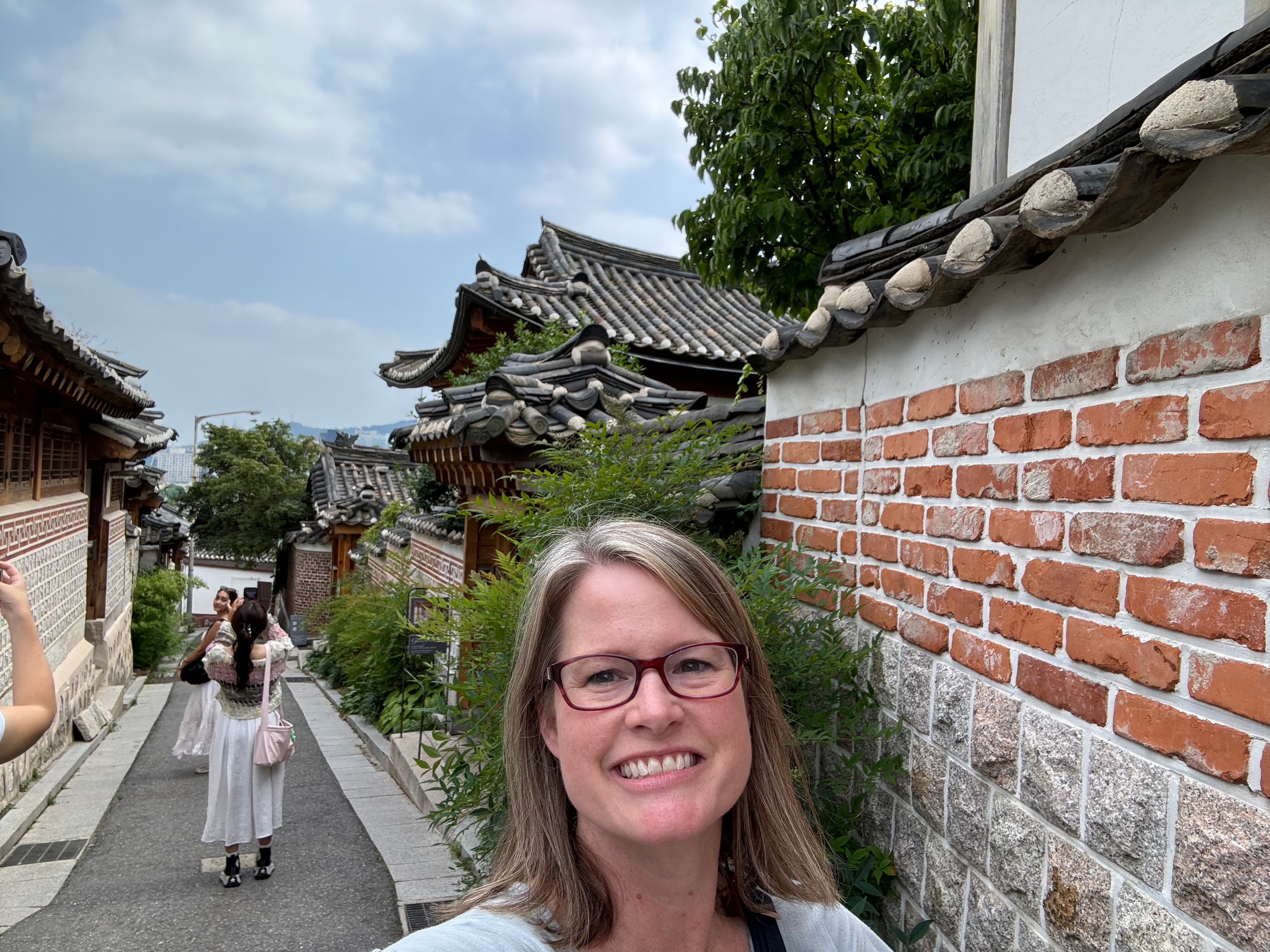 Advisor taking a selfie by a brick wall and a few trees on a sunny day