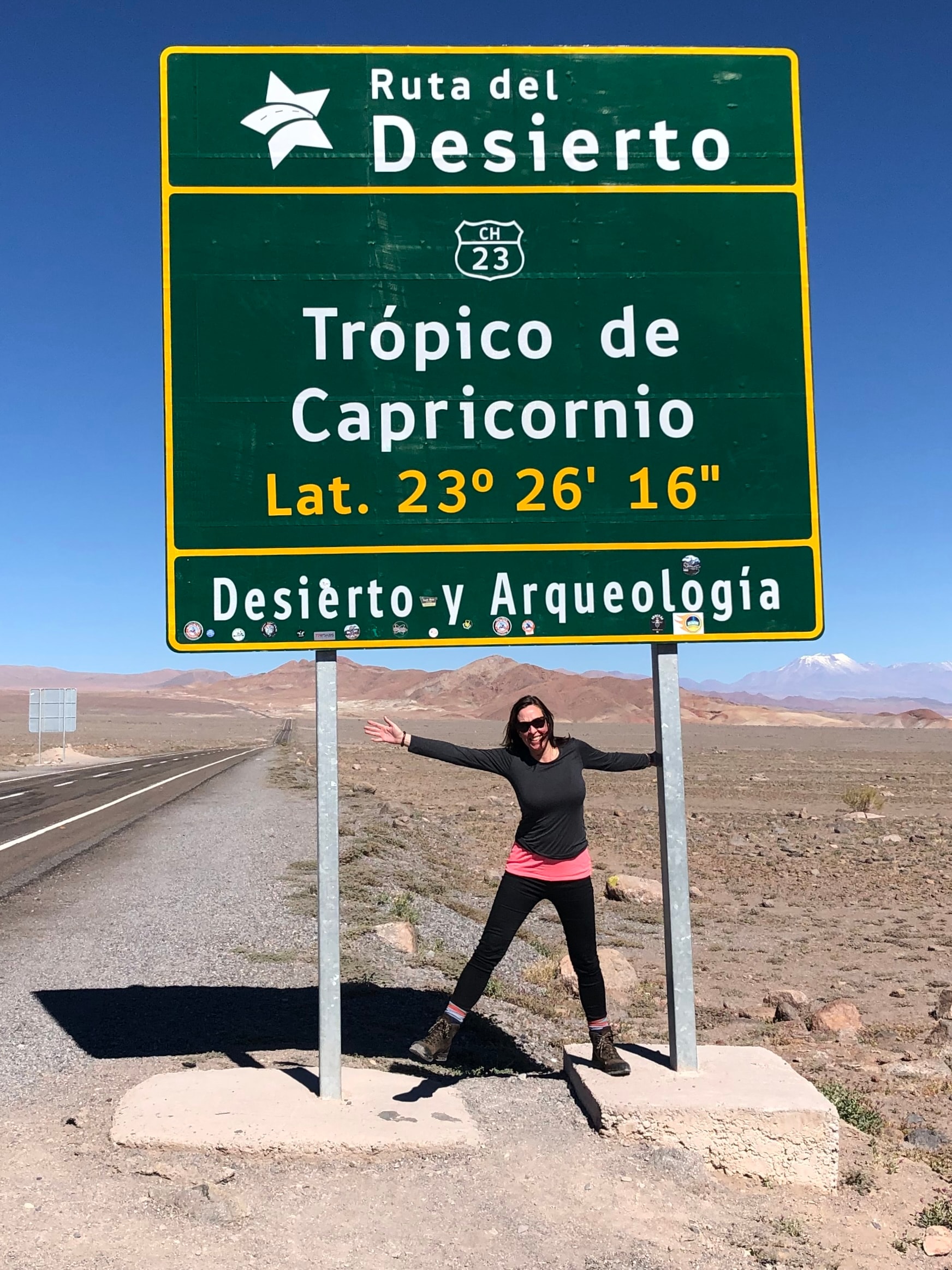 Jill posing underneath a large sign for the Tropic of Capricorn on a sunny day