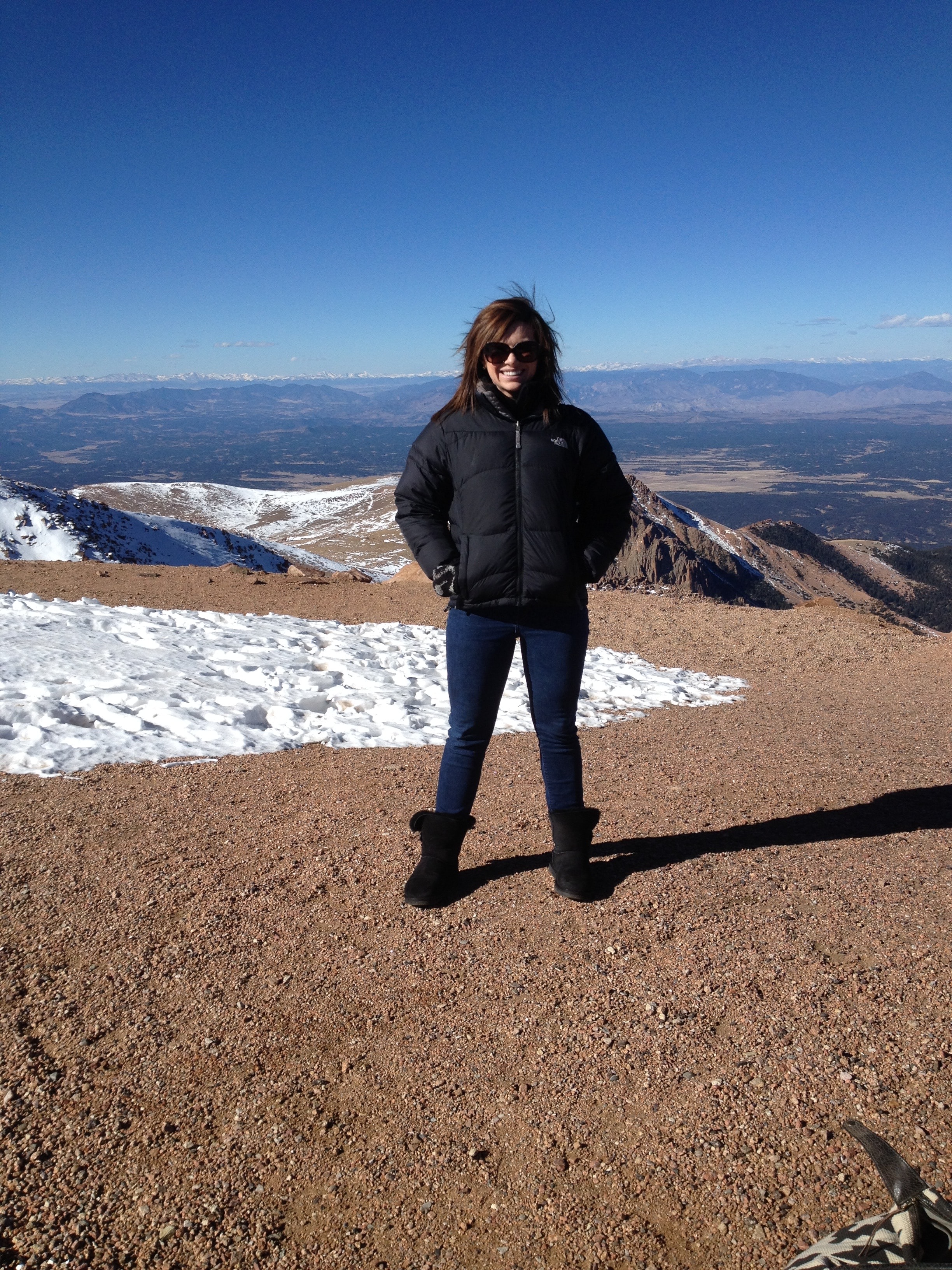 Travel advisor Sarah Rash standing at a high point overlooking mountains against a bright blue sky.