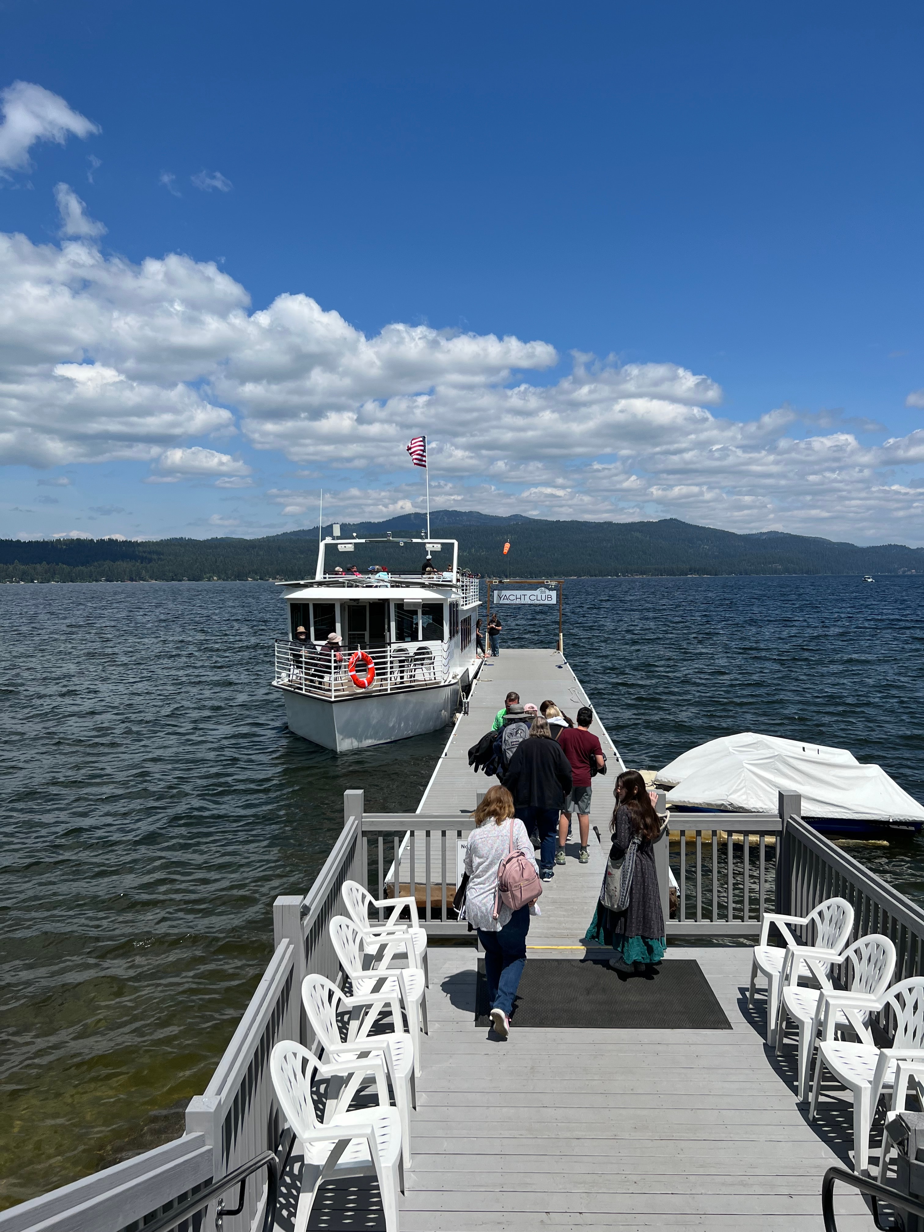 View of several people walking on to a dock with a boat at the end on a sunny day