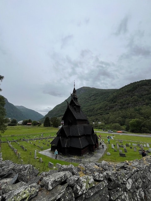 A tall building in the center of the green grass and mountains.