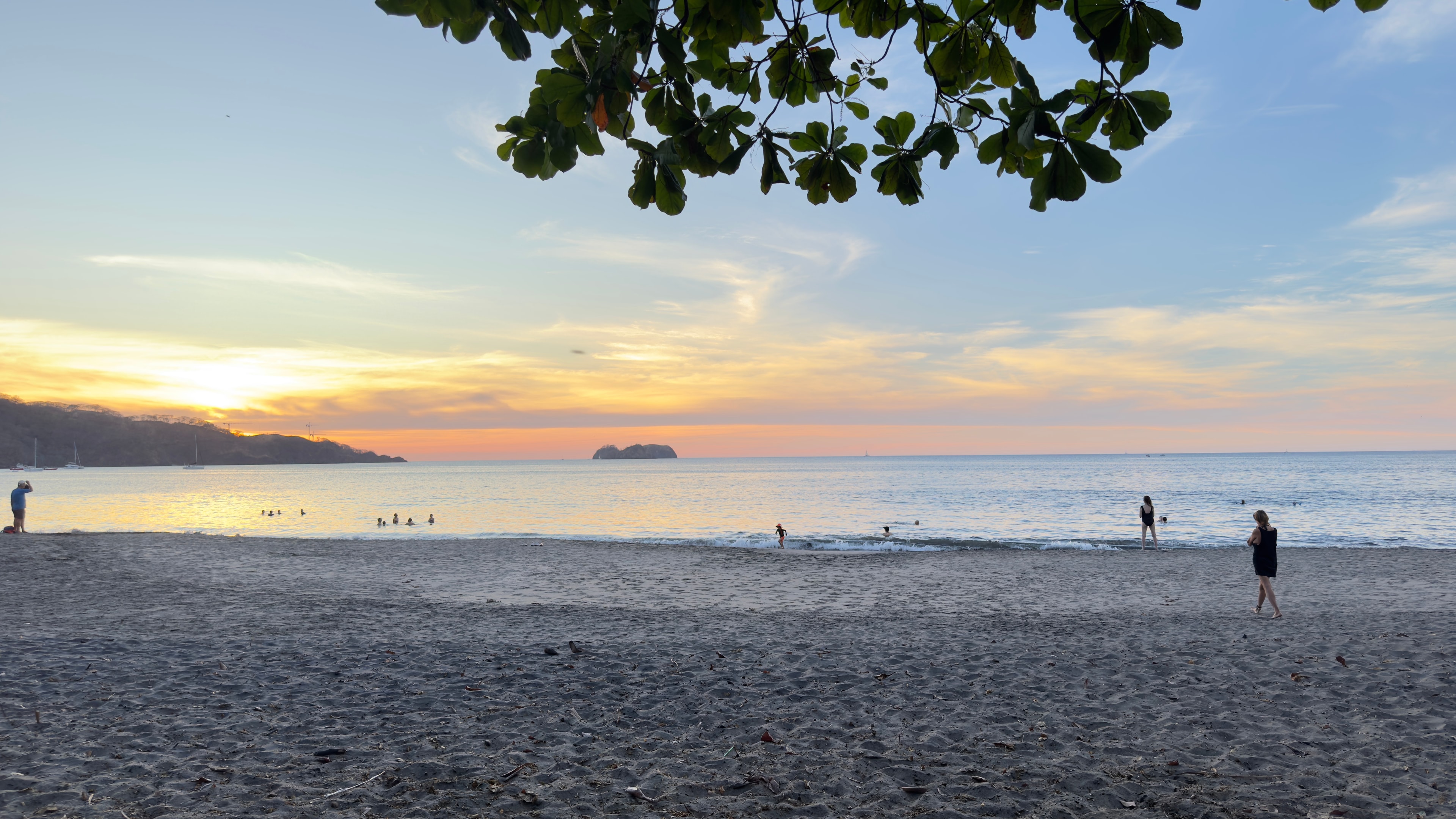 View of a wide beach and a calm ocean with a few people walking by at sunset