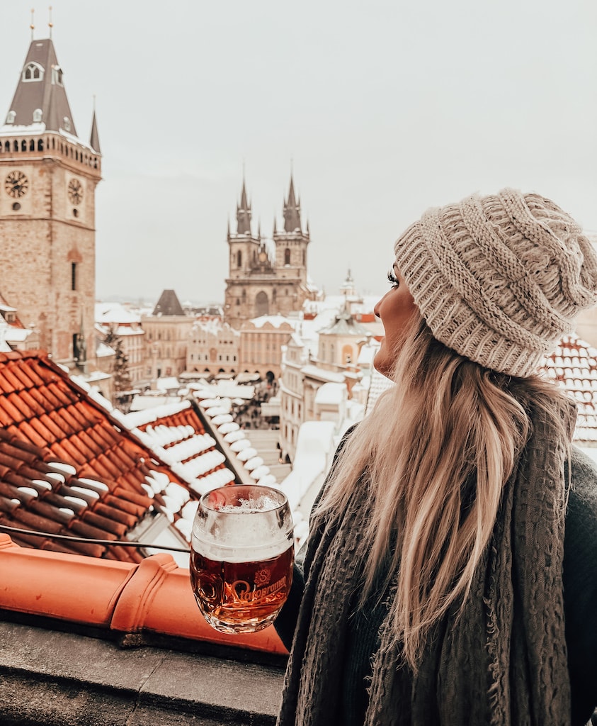 Advisor in a knit hat holding a mug of beer on a balcony overlooking the Prague skyline