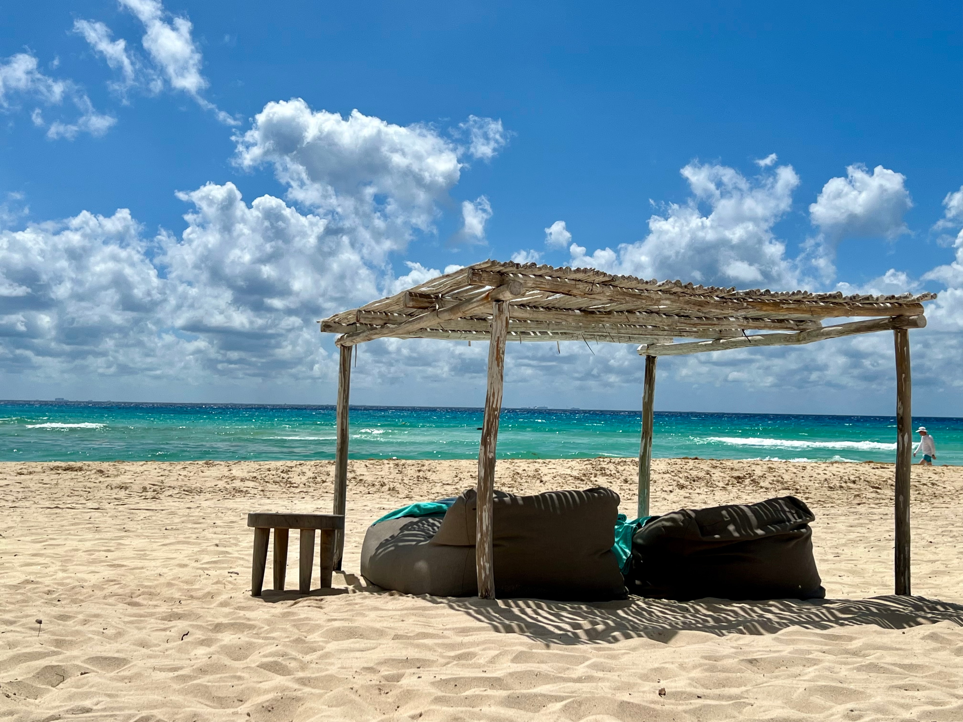 Bean bags on the beach under a thatched roof with blue water.