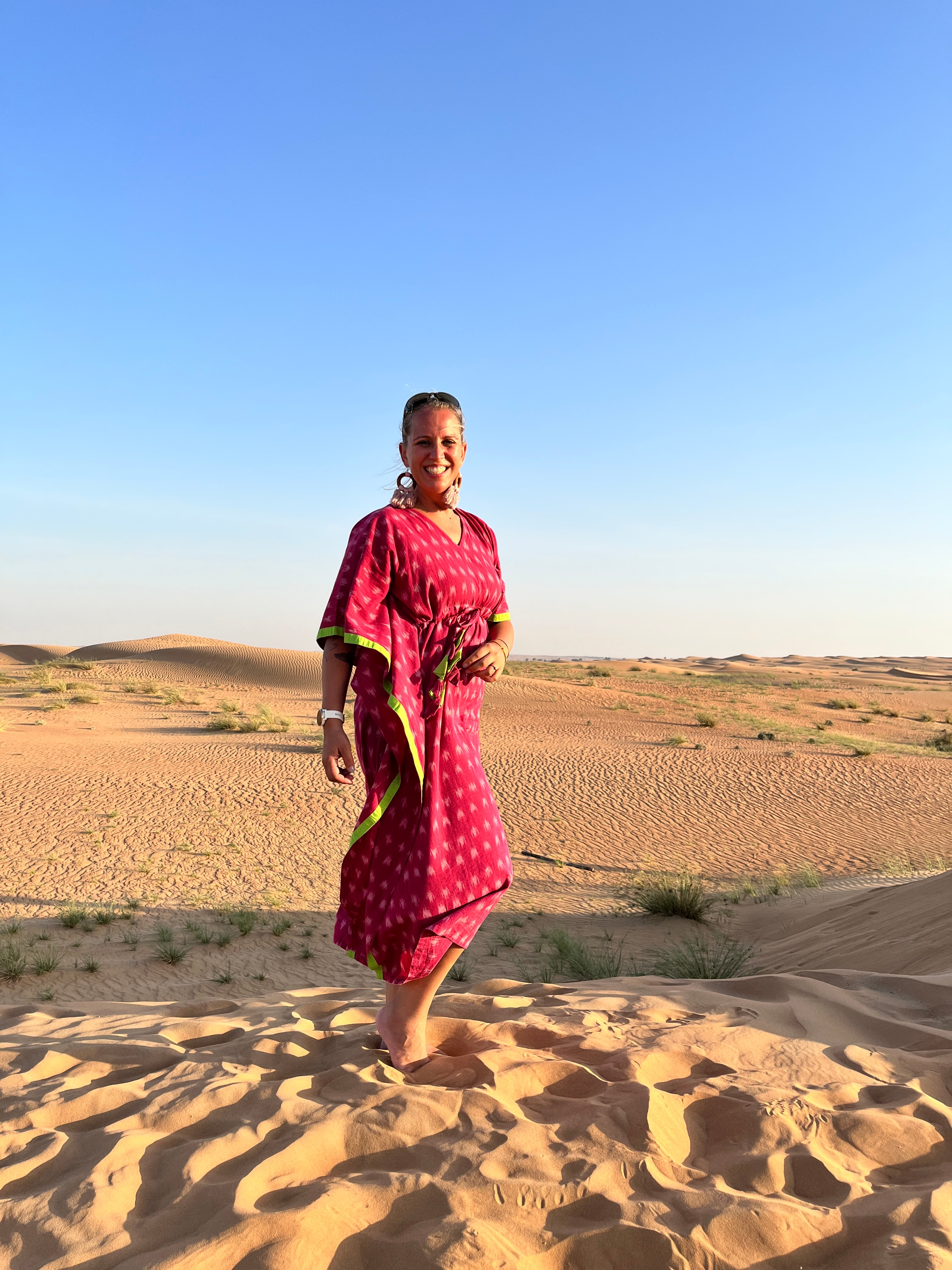 Advisor in a pink dress standing barefoot in the desert under clear skies