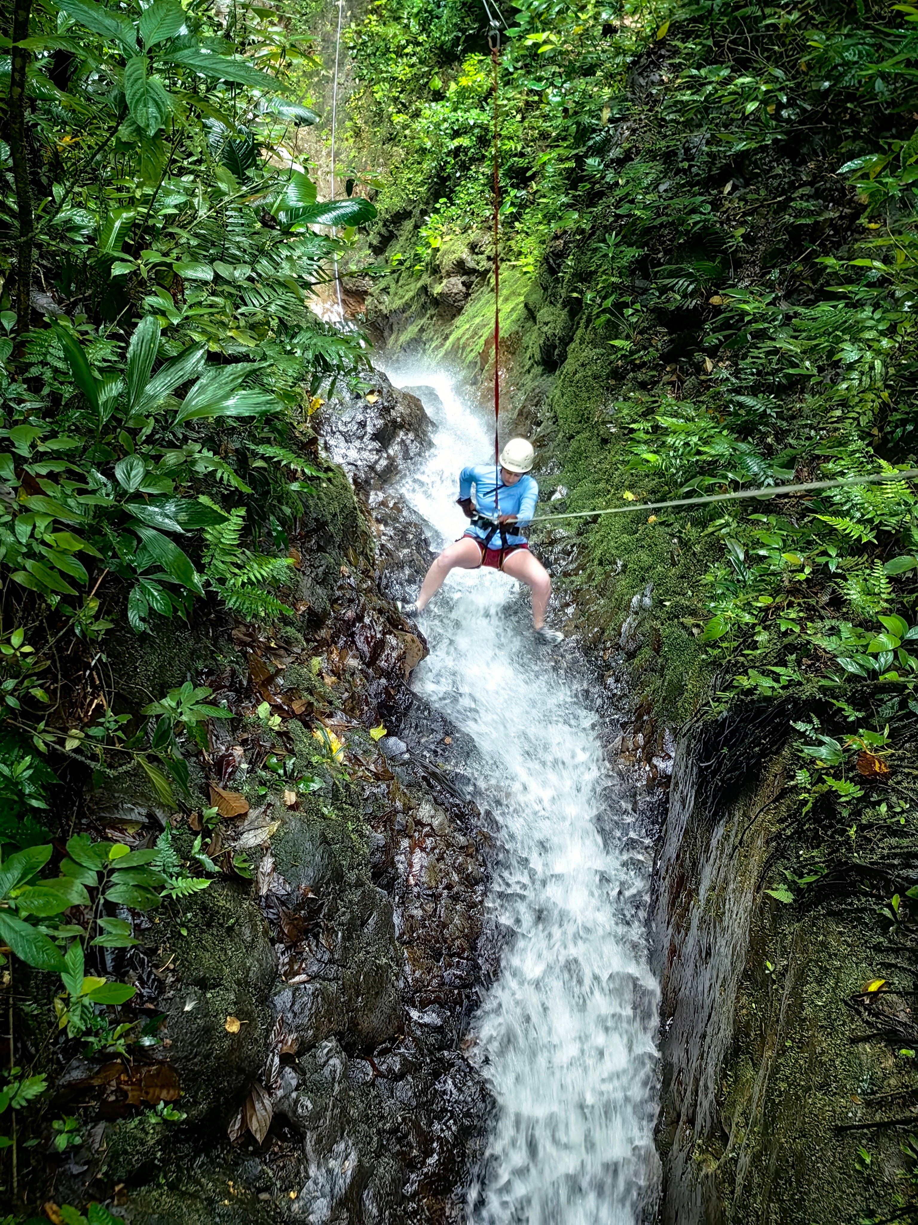 View of advisor zip lining across a waterfall in the jungle