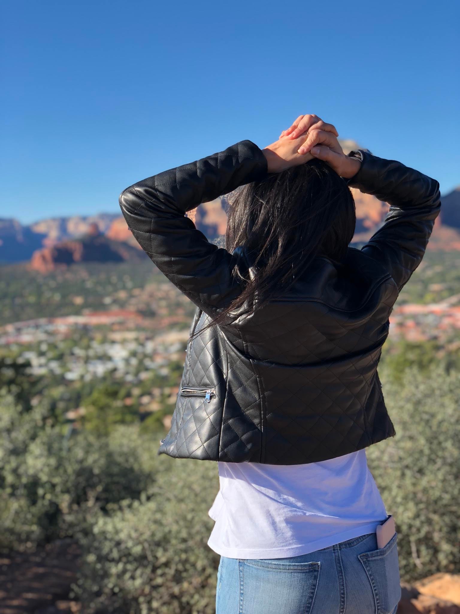 Advisor in a leather jacket looking out towards a green valley with mountains in the distance on a sunny day