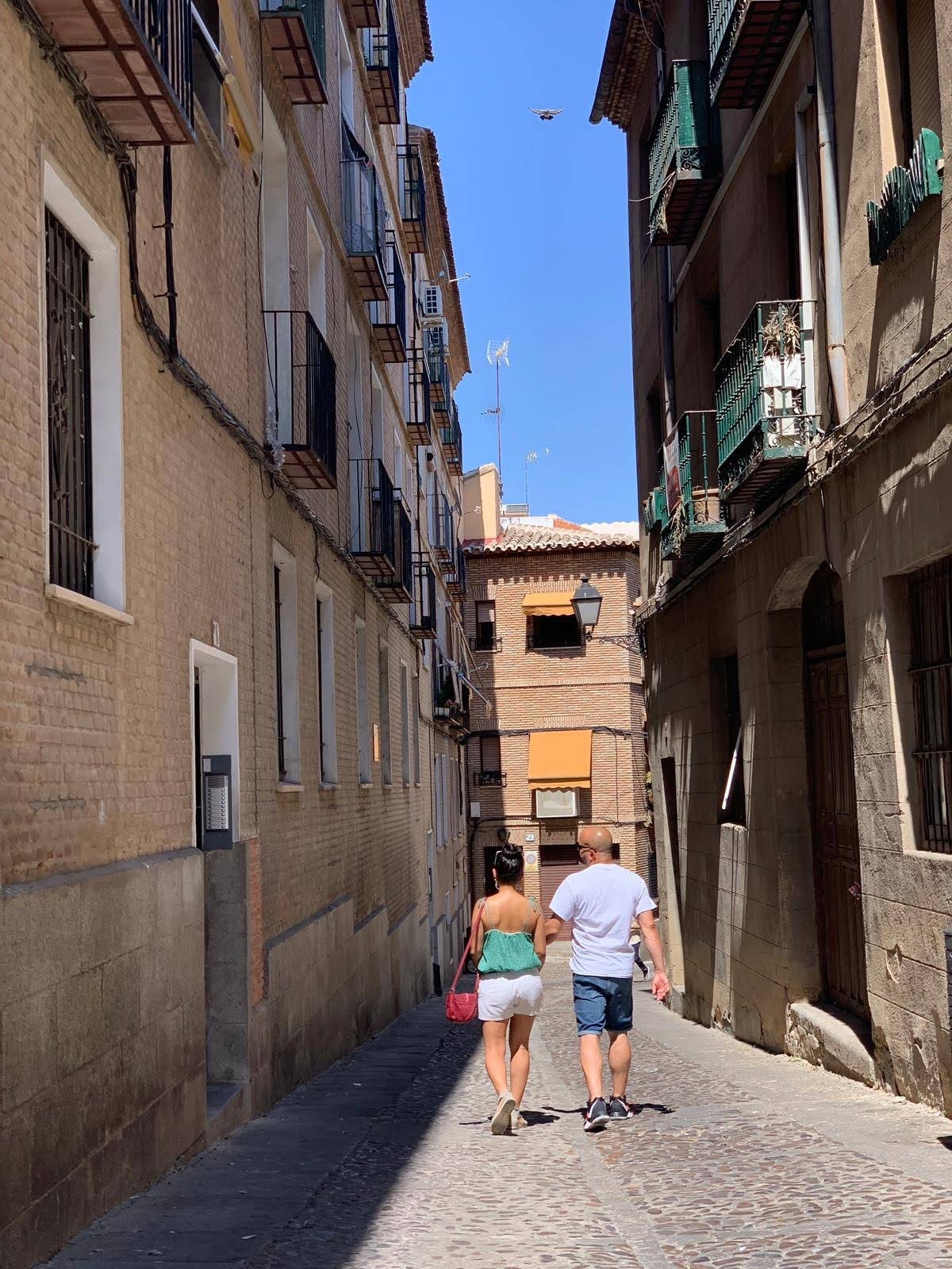 Two people walking arm in arm down a narrow city street on a sunny day