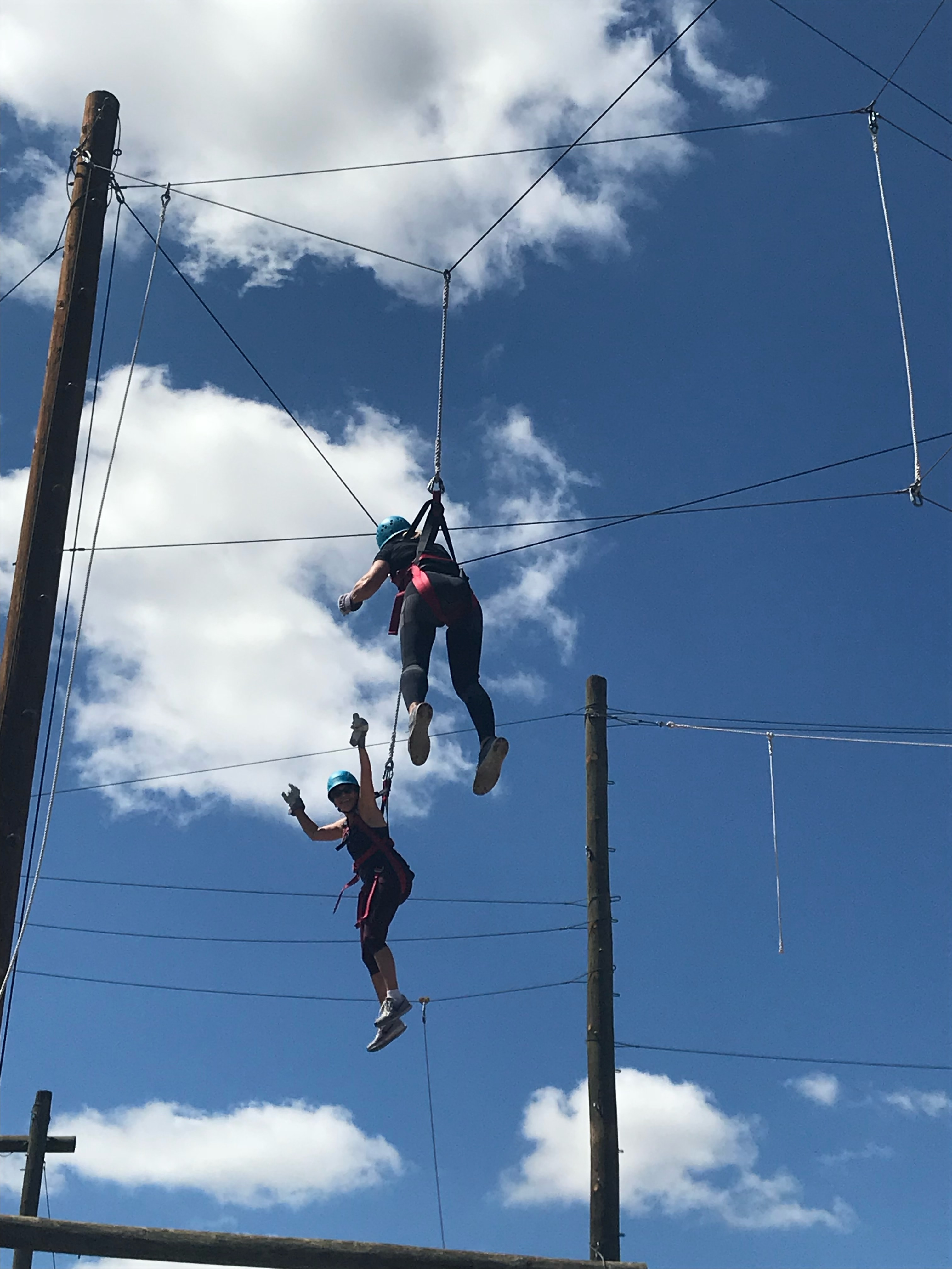 View of two people in harnesses jumping on a trampoline outdoors on a sunny day