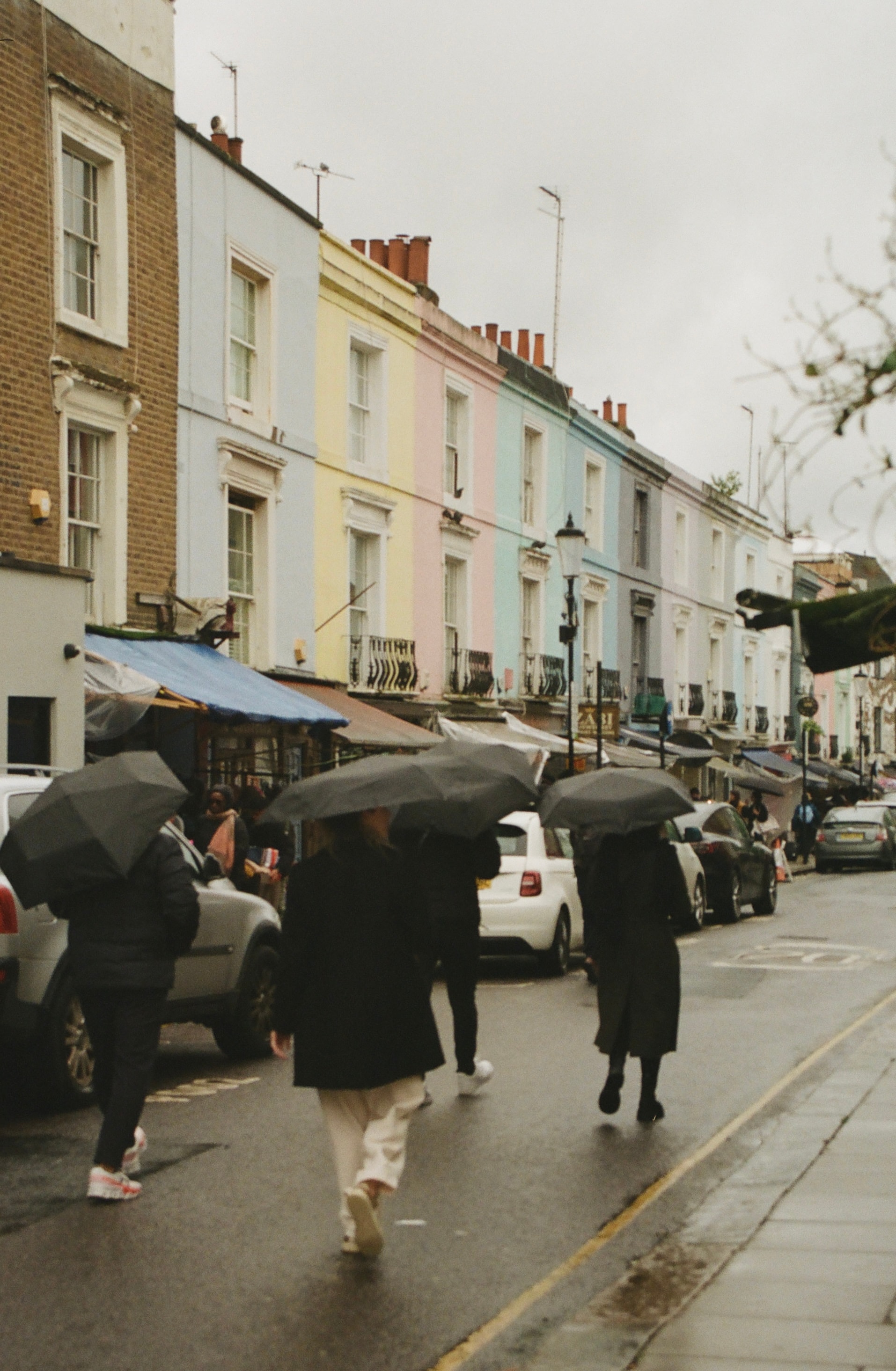 View of people in black coats walking down a rainy street with black umbrellas overhead