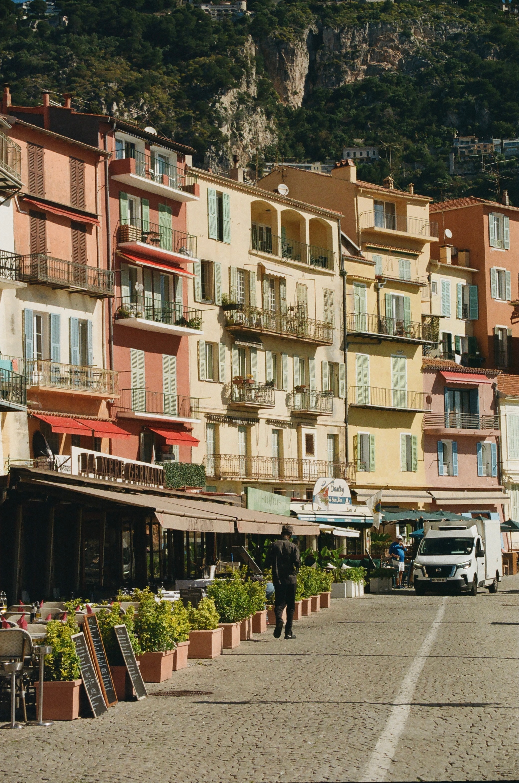 View of a small street lined with colorful apartment buildings and green mountains visible behind