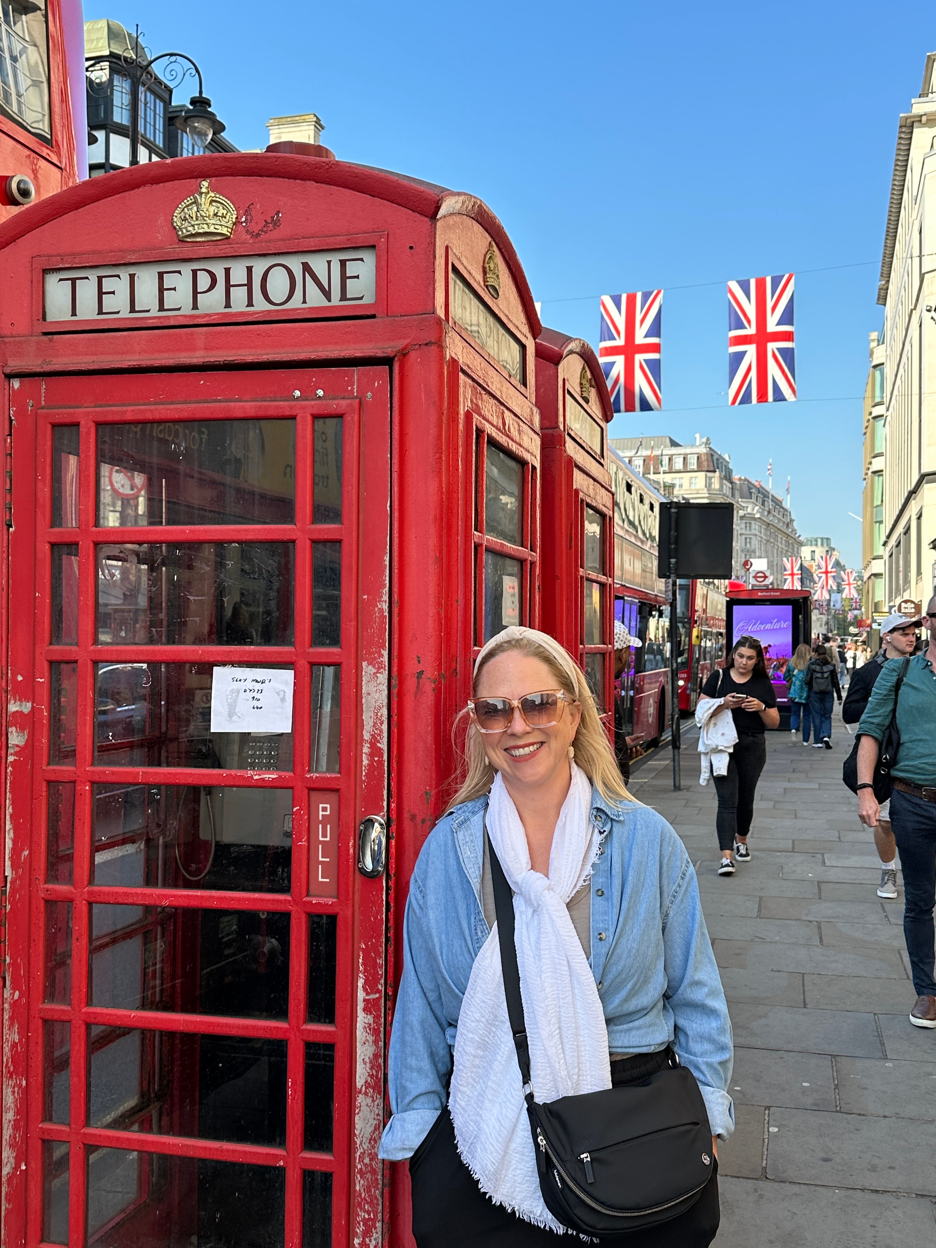 Advisor posing besides a red telephone booth in England on a sunny day