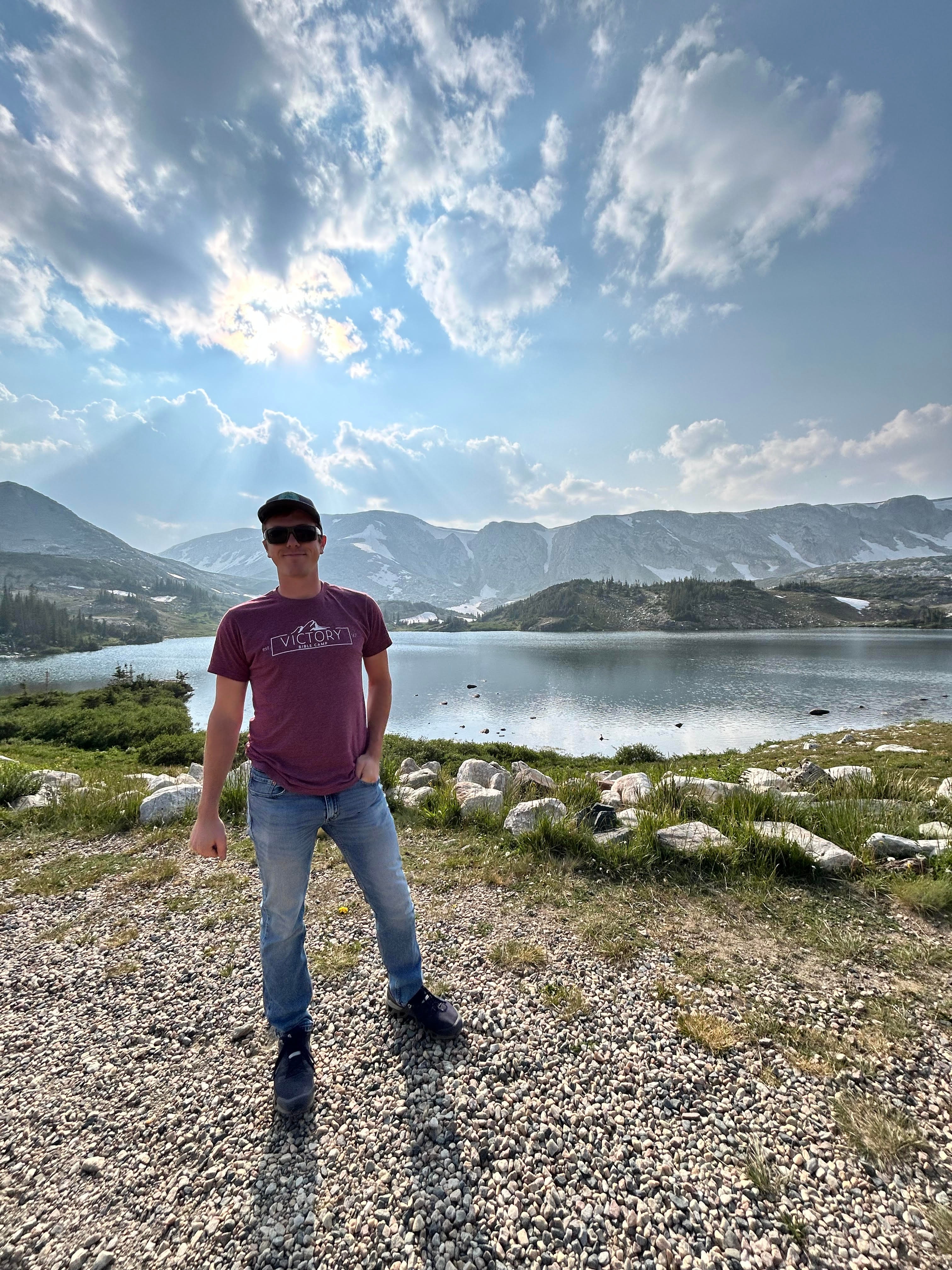 Advisor posing by glassy lake surrounded by mountains on a sunny day