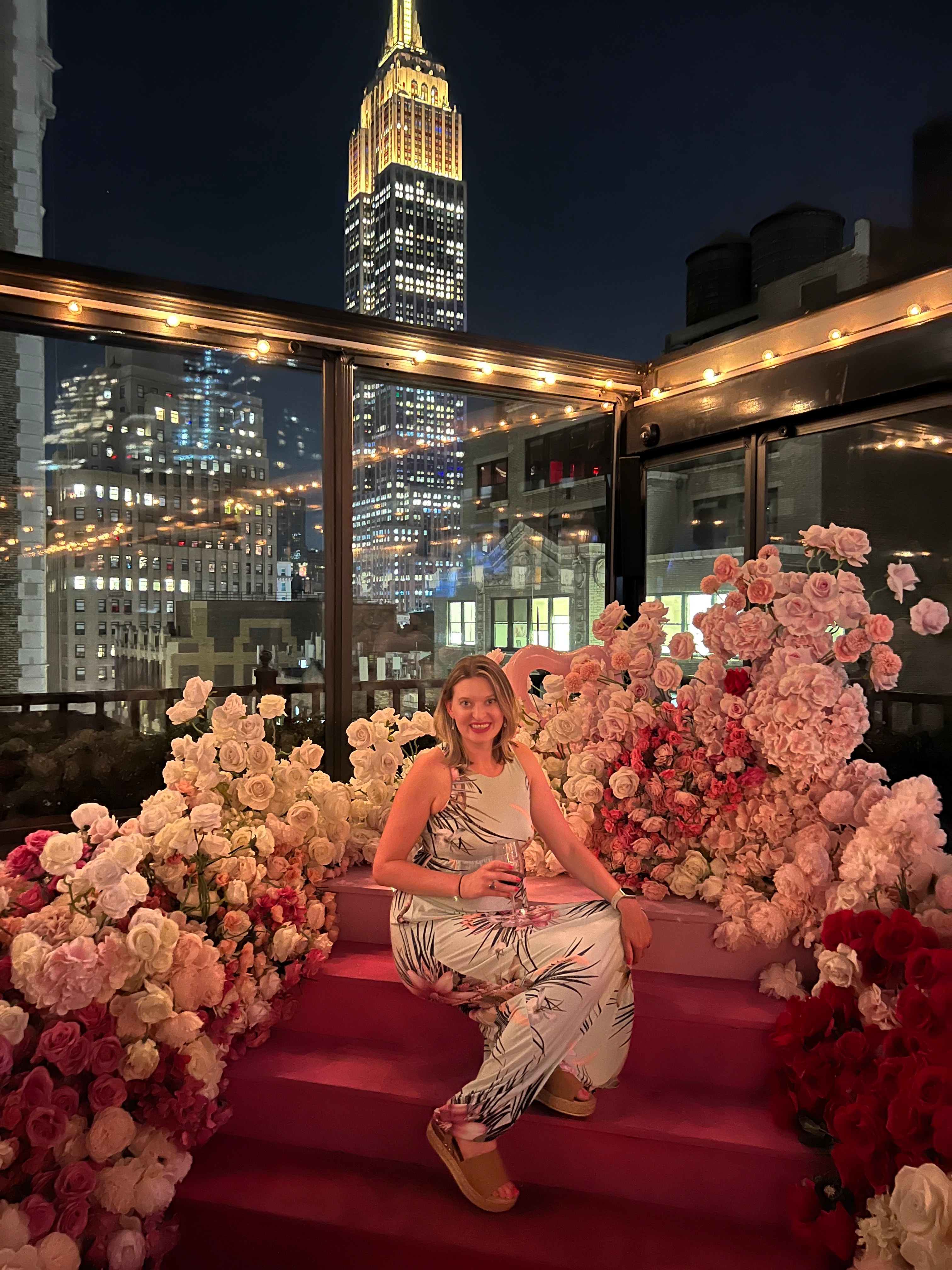 Advisor sitting on red stairs decorated with a display of pink flowers on a NYC rooftop at night