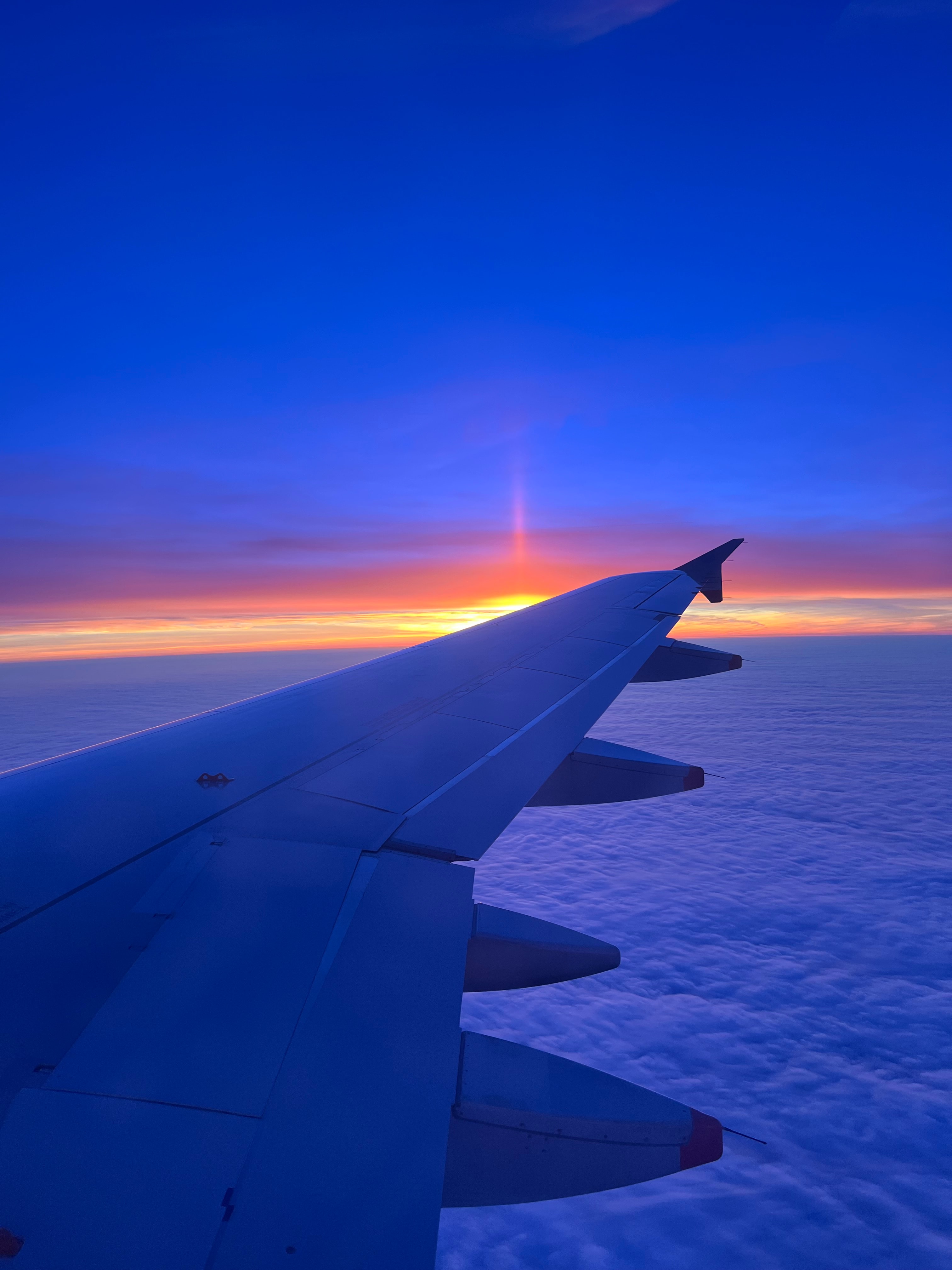 View of a plane wing in the sky against a bright sun on the horizon