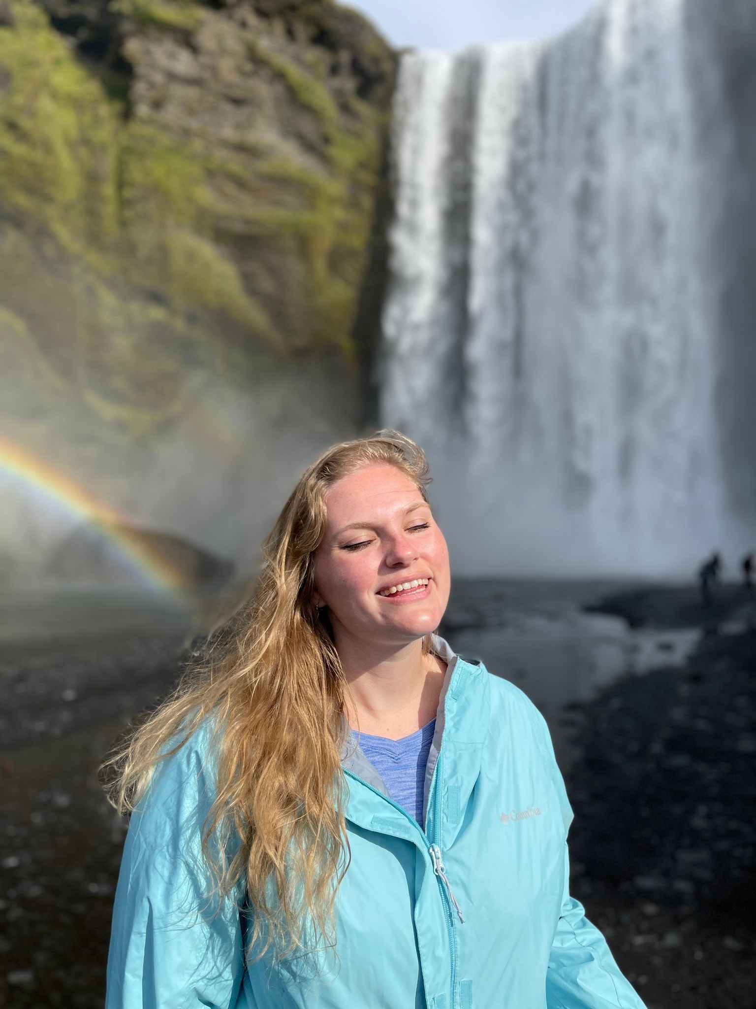 Advisor in a blue windbreaker jacket smiling in front of a large waterfall