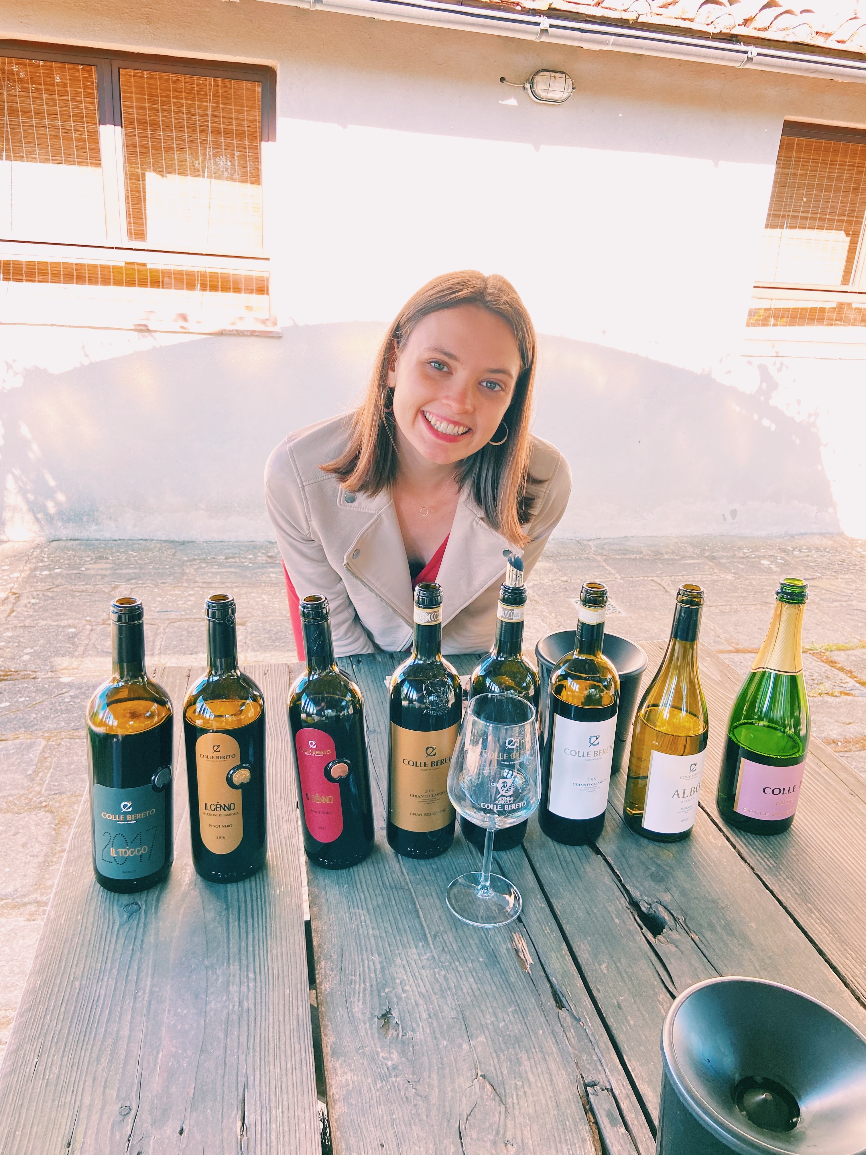 Advisor smiling behind a line of wine bottles set on a wooden table outdoors 