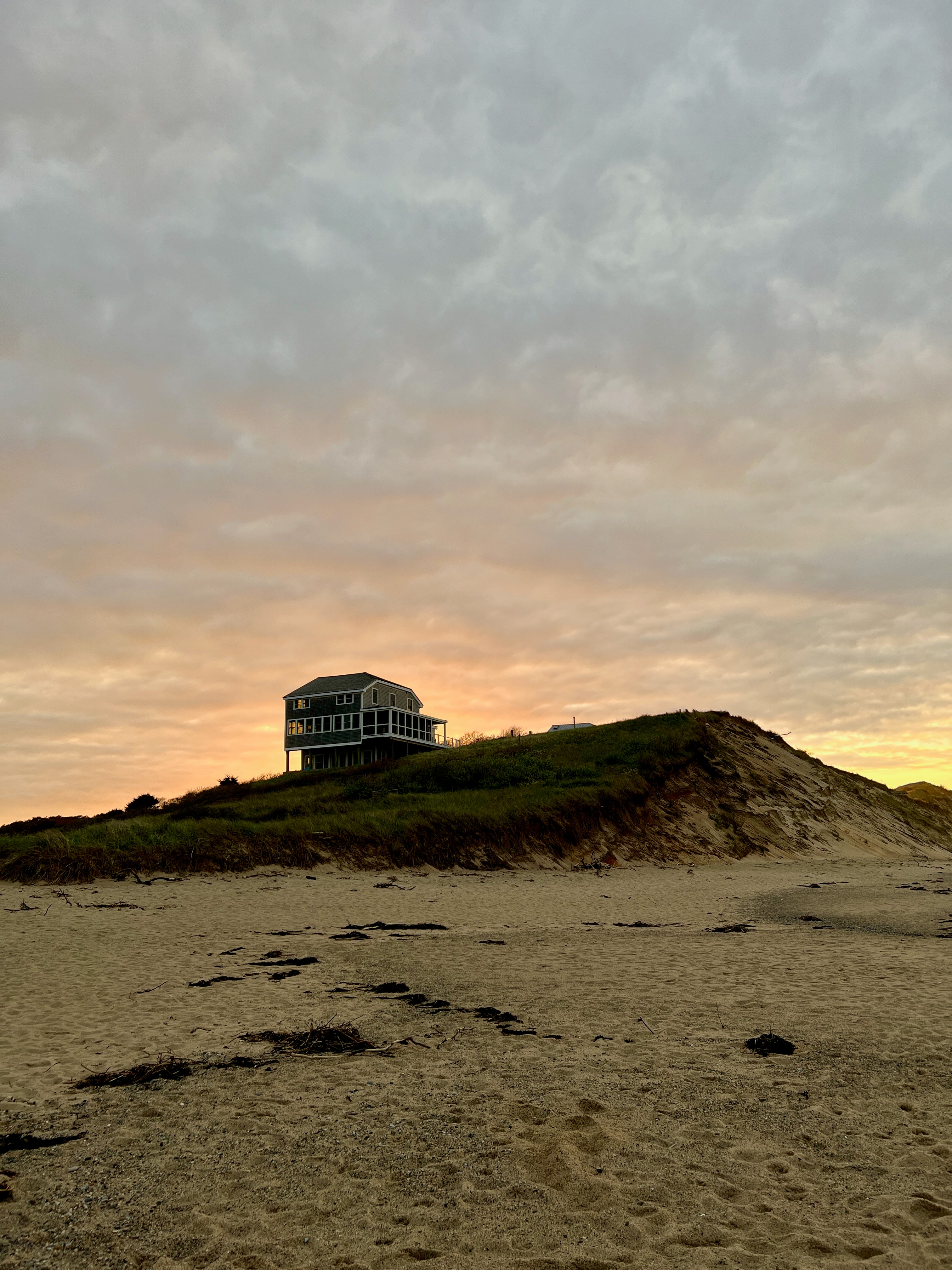 A view of a house on the top of a hill at sunset with a beach in the distance. 