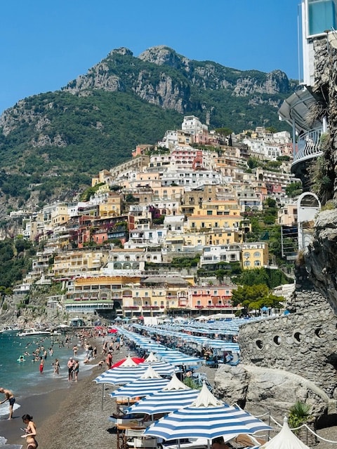 View of a colorful coastal town and beach with blue and white striped umbrellas on a sunny day