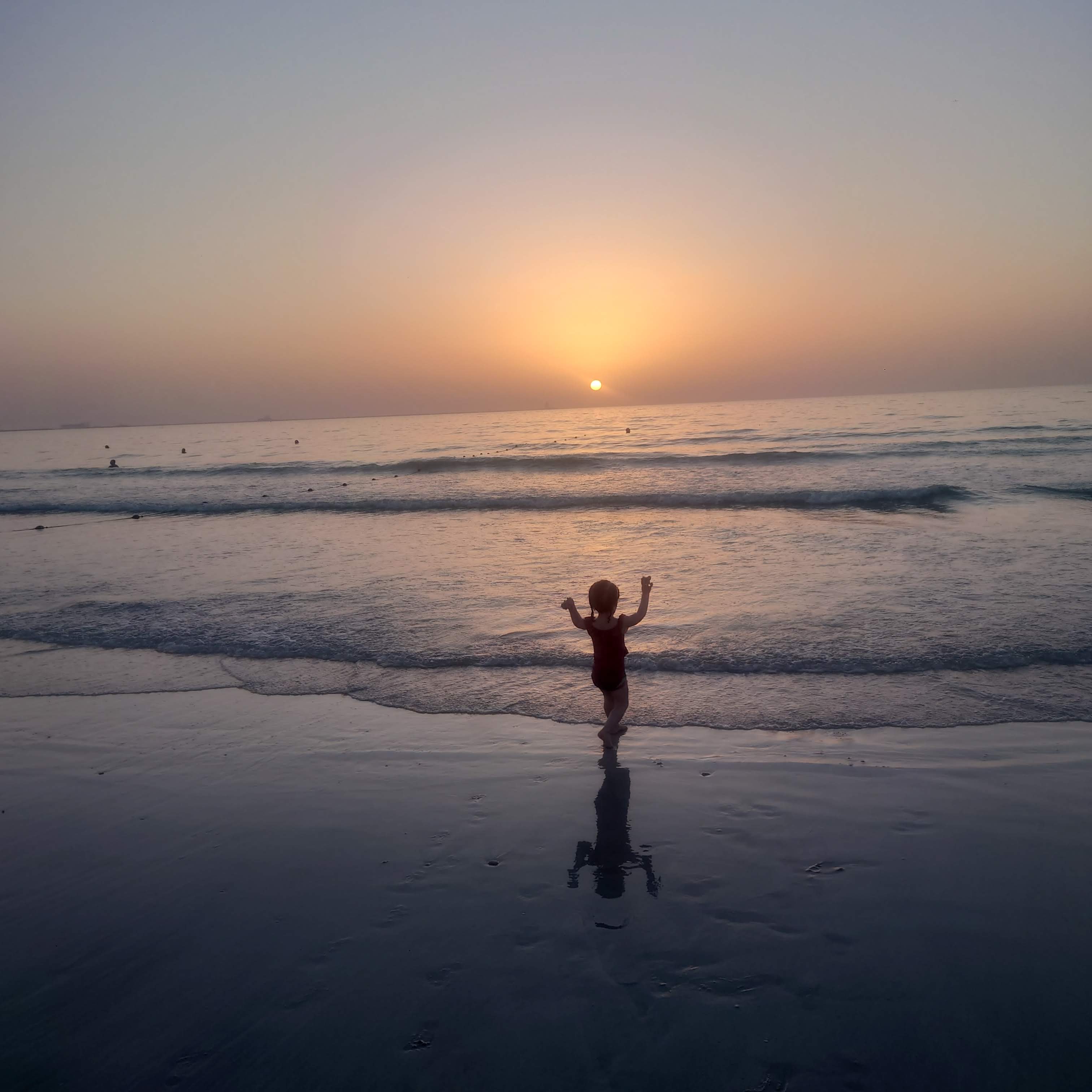 View of a small child running towards the sea at sunset