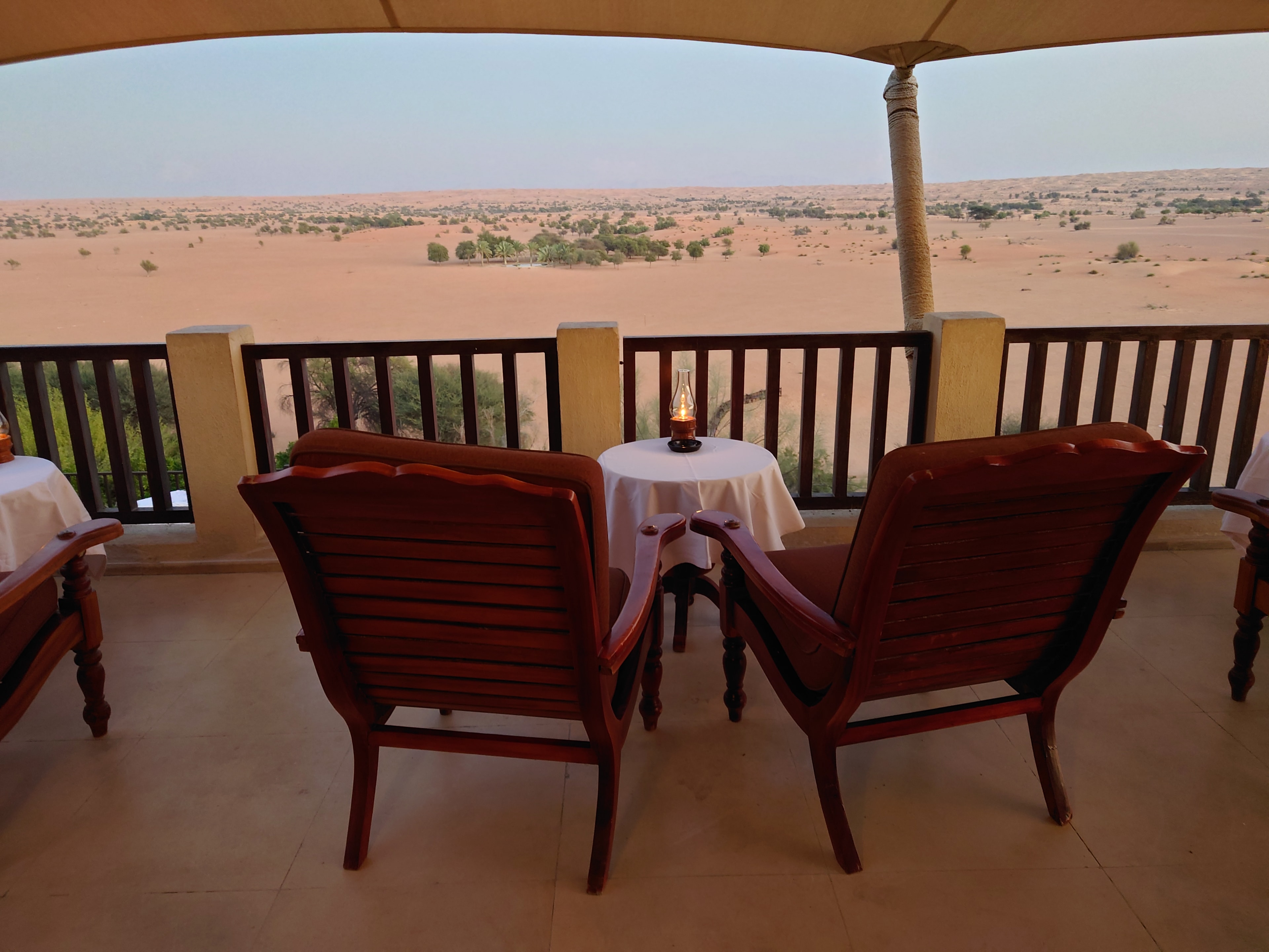 Two red chairs and a small round table on a deck overlooking a desert environment