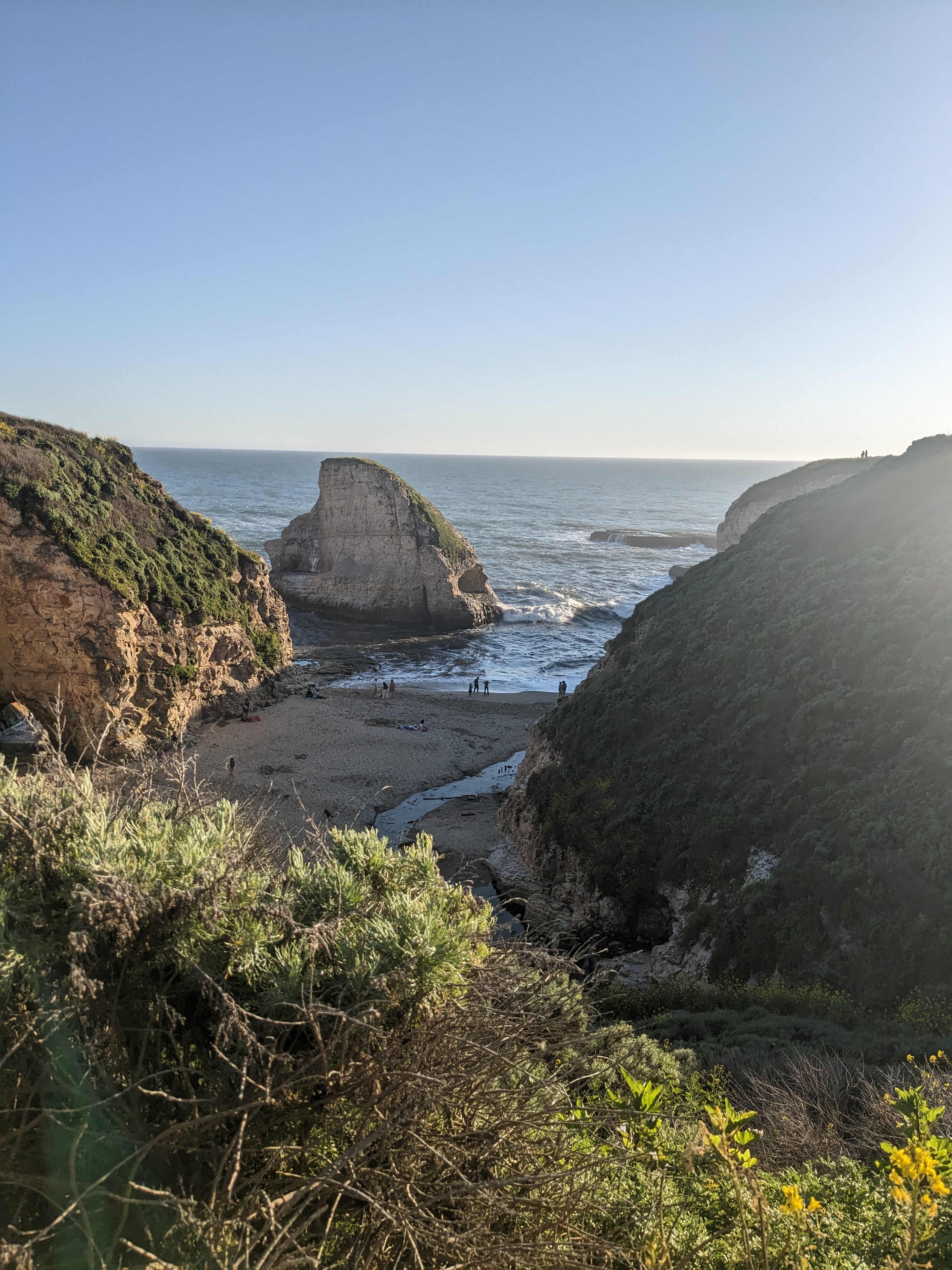 A view of a rocky beach and natural foliage positioned in front of the blue sea. 